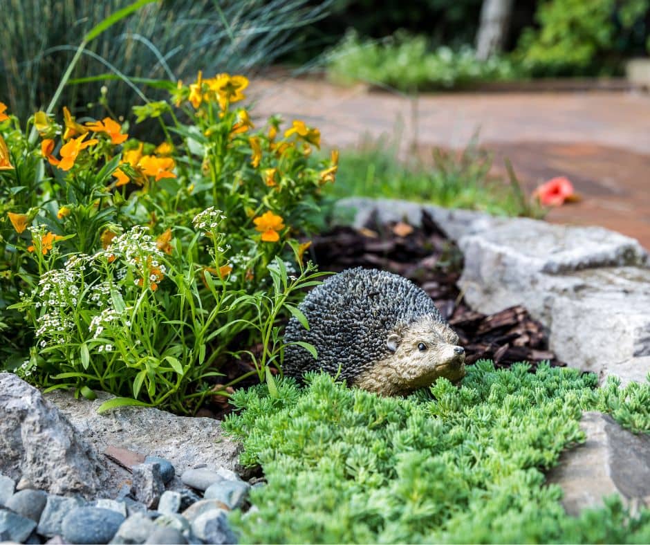 A groundhog sculpture in a sunny bed of mixed plants.