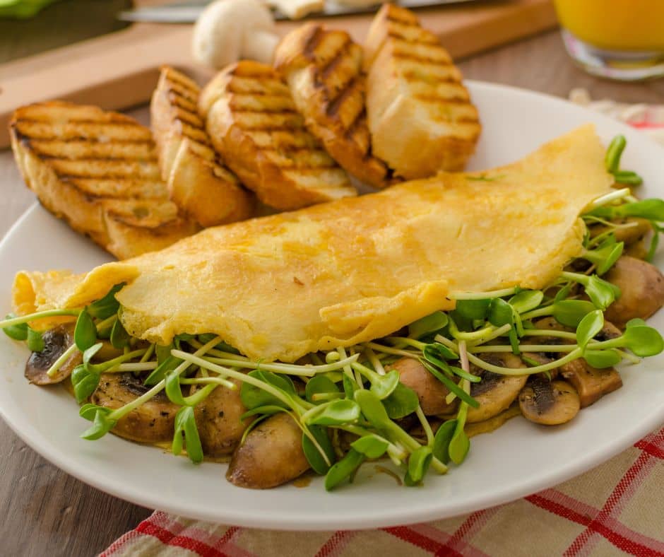 A mushroom and sunflower microgreen omelet on a white plate with toast.