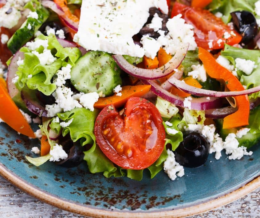 Fresh mixed salad with crumbly white feta cheese on a blue plate.
