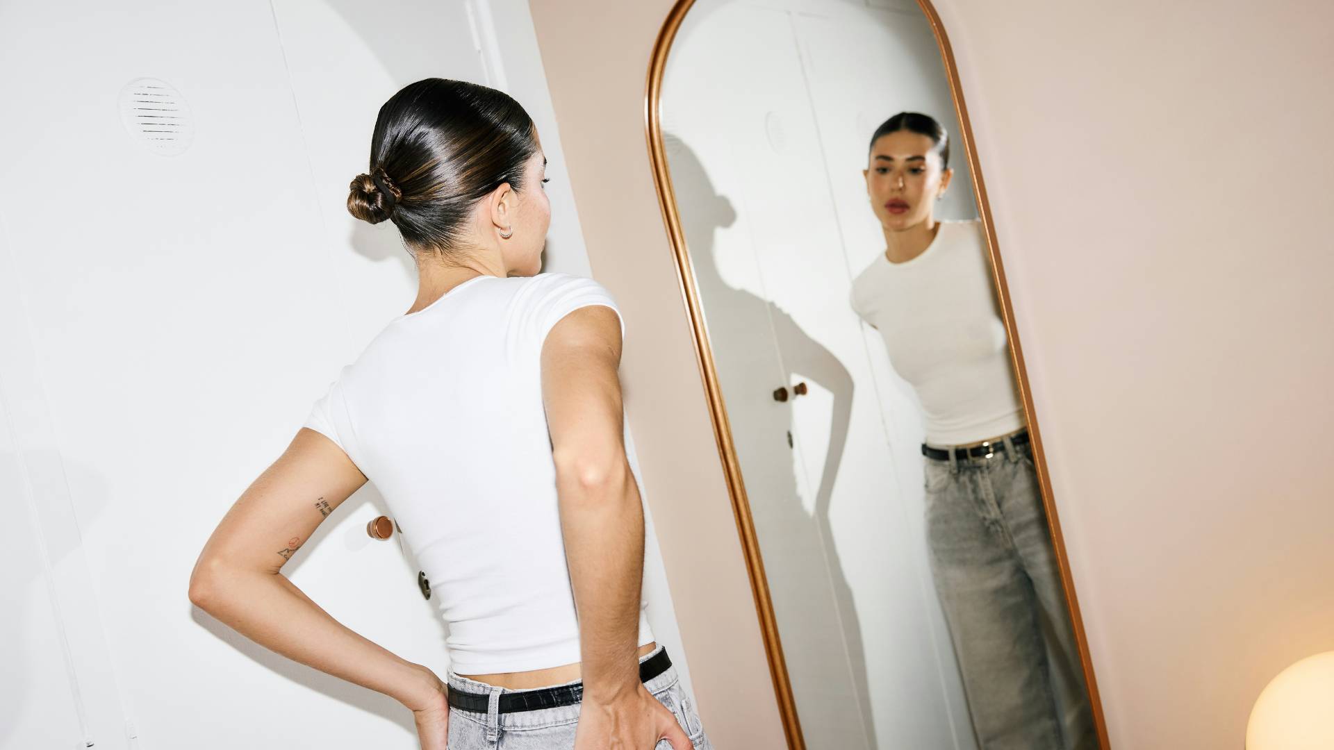 woman with dark hair and white shirt looking in the mirror