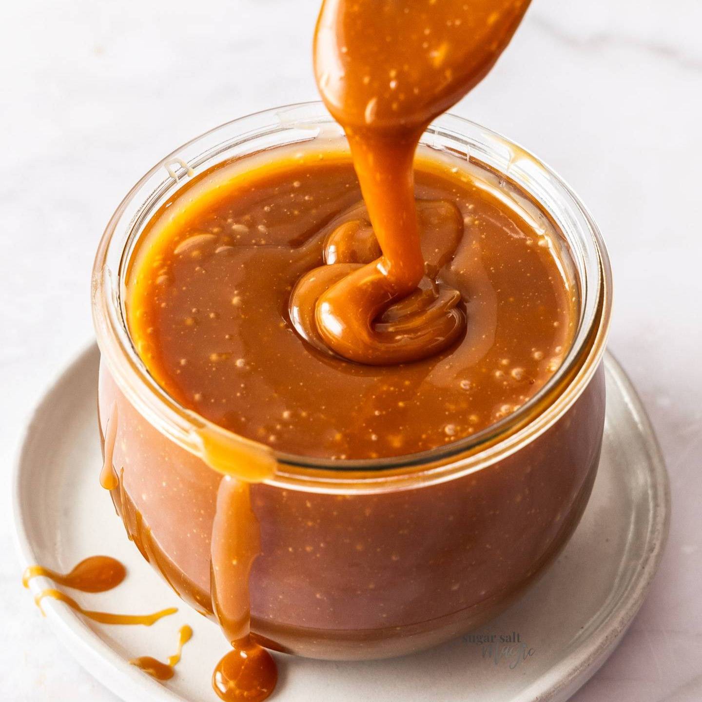 Caramel drizzling off a spoon into a jar of caramel.