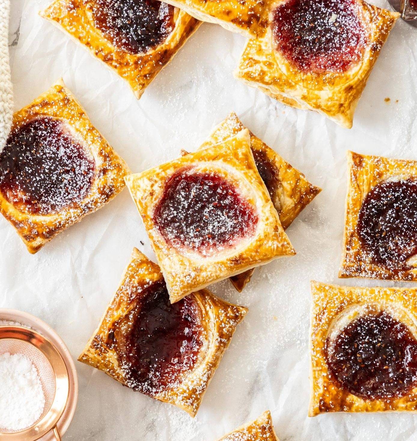 A batch of square jam tarts on a sheet of baking paper.