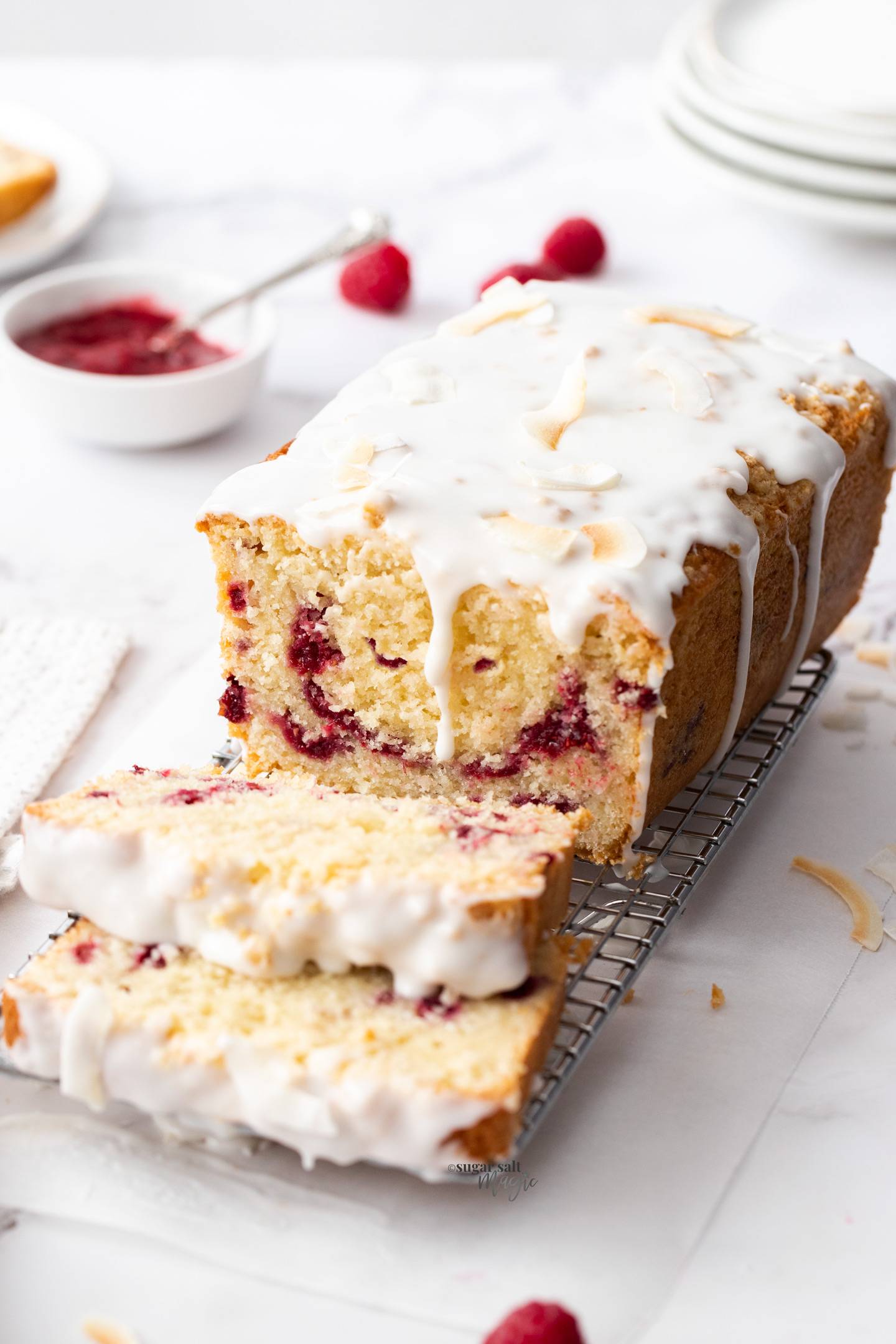 A coconut raspberry loaf cake on a metal rack with two slices cut.