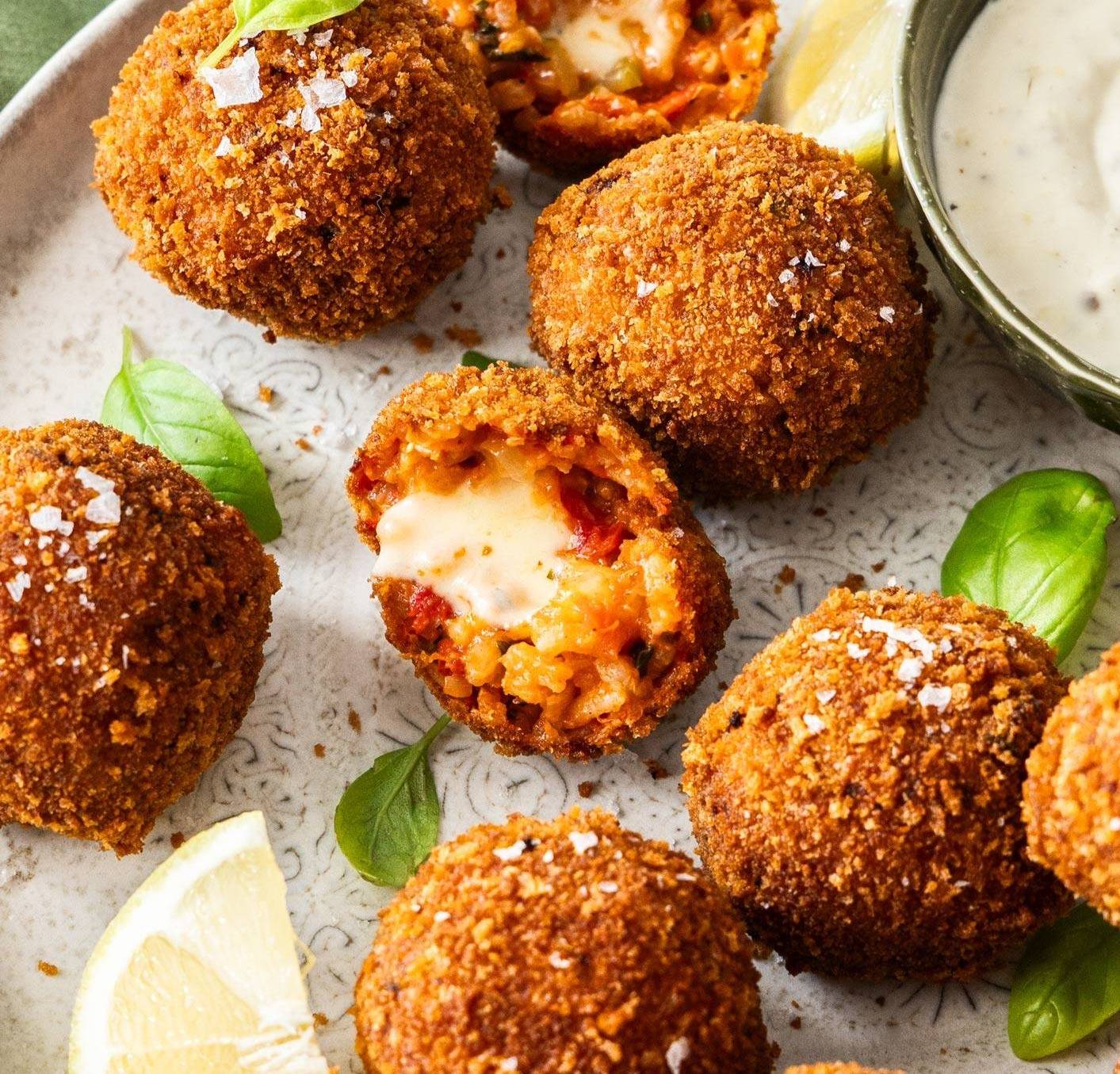A plate topped with golden brown arancini balls with one torn open to show the cheesy filling.