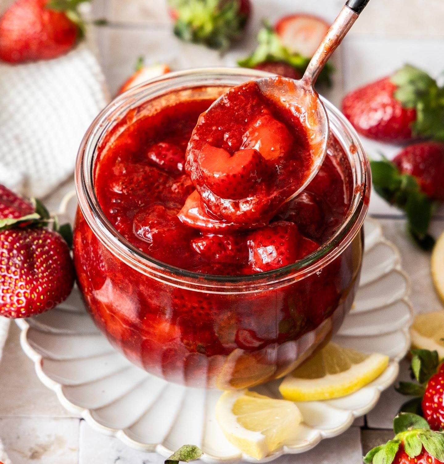 A spoon taking strawberry compote out of a glass jar.