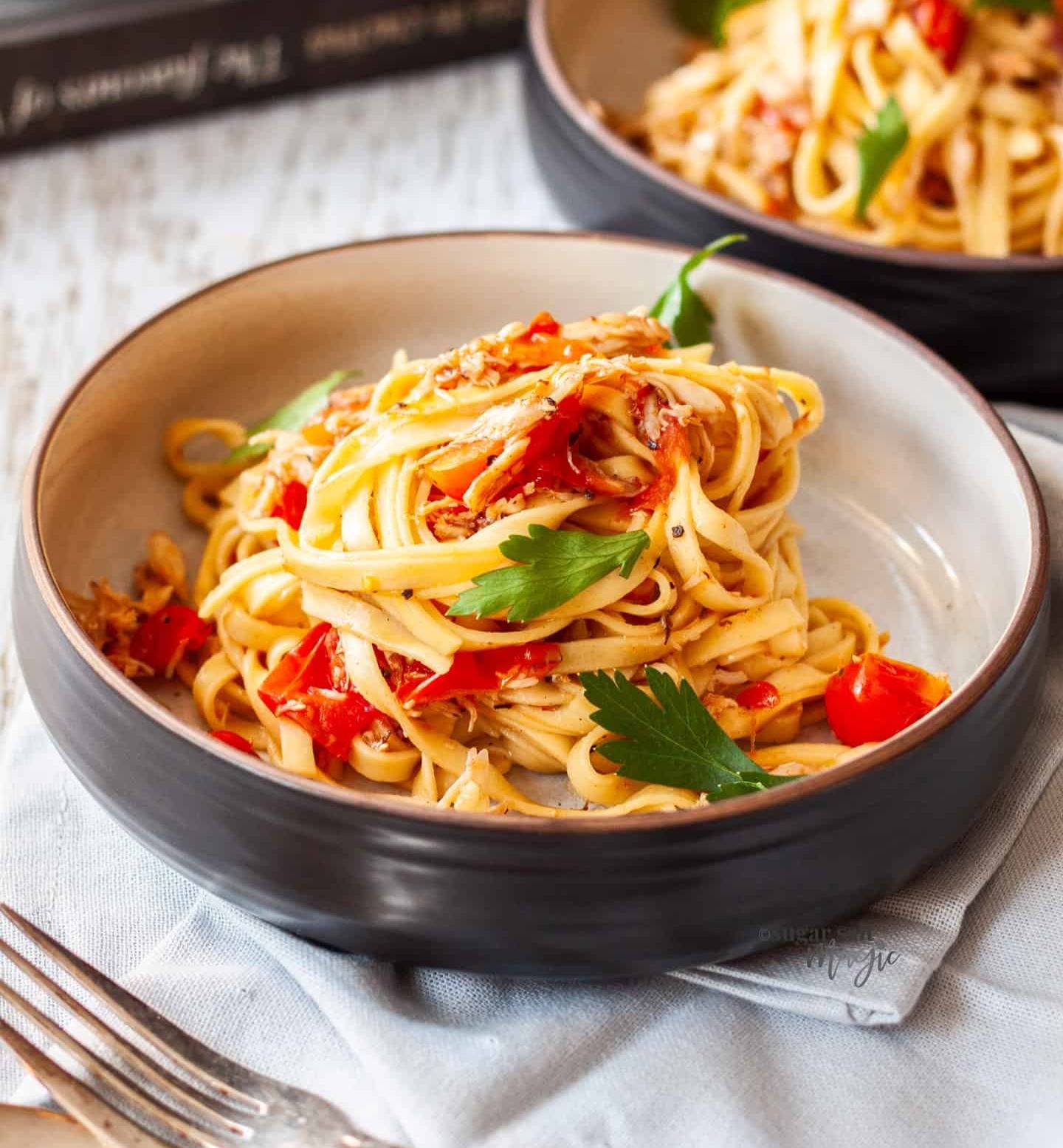 A bowl filled with linguine, tomatoes and crab.
