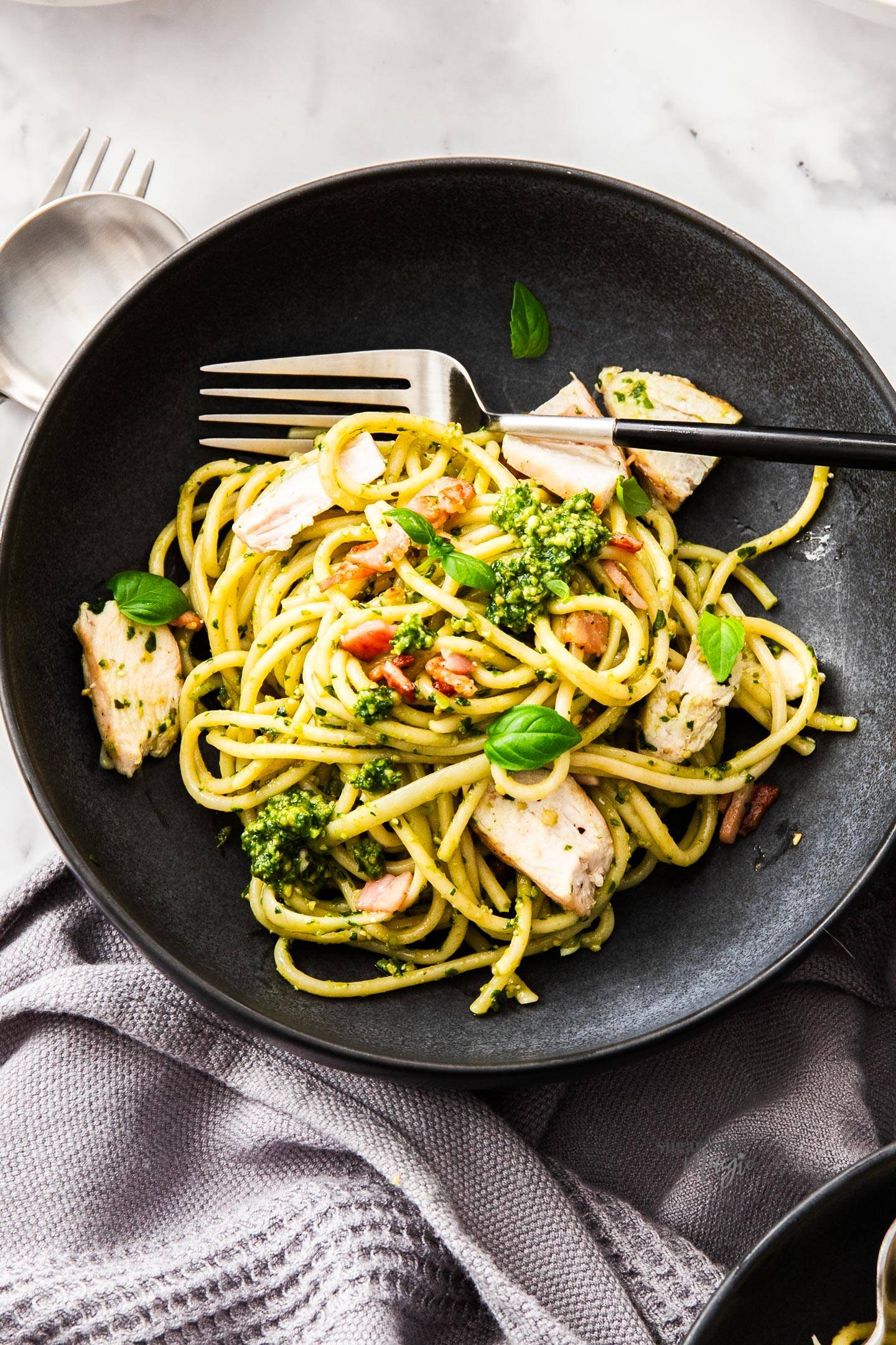 Top down view of a black bowl filled with pesto chicken and spaghetti.