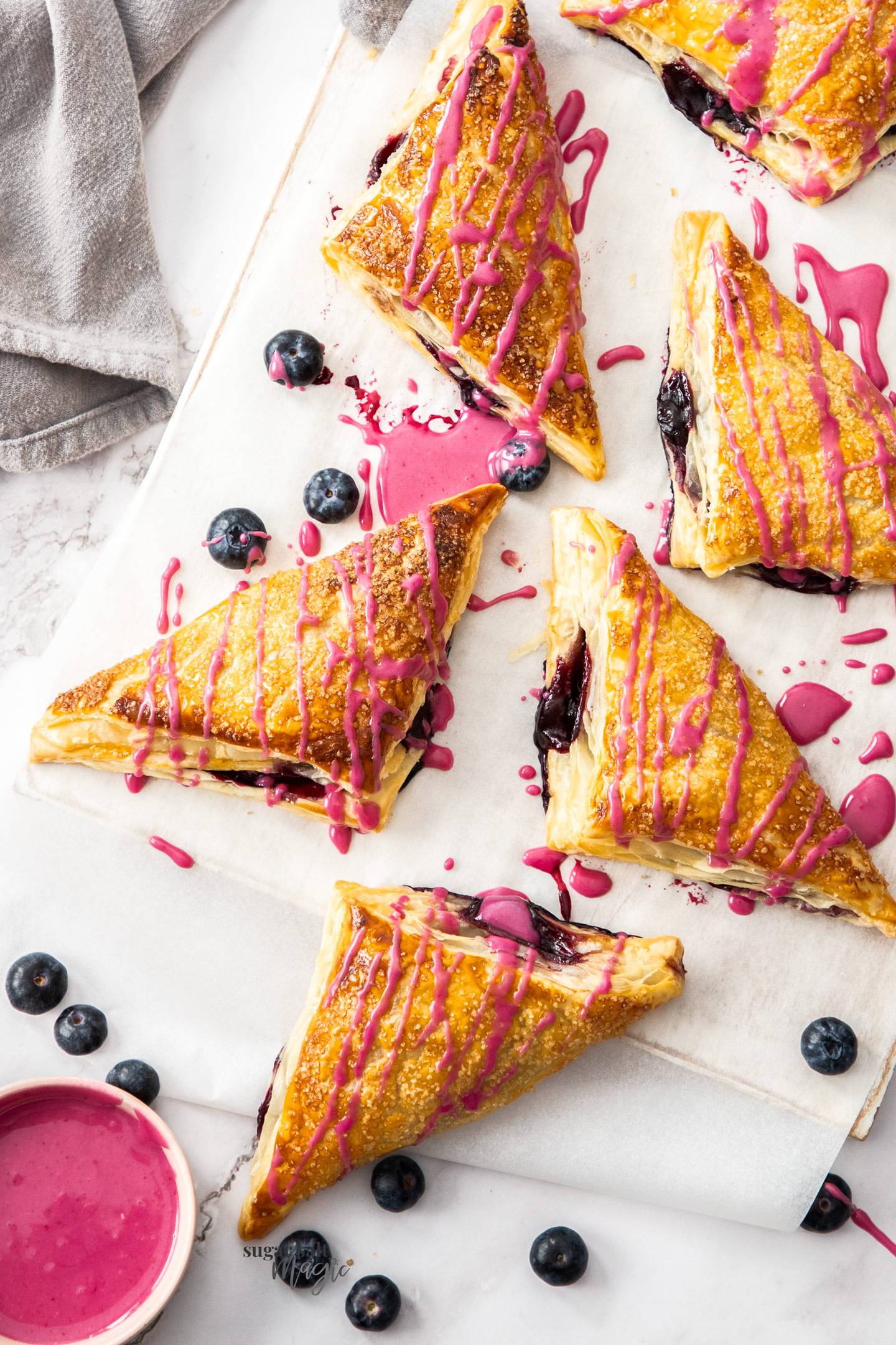A batch of blueberry pastries drizzled with pink glaze.