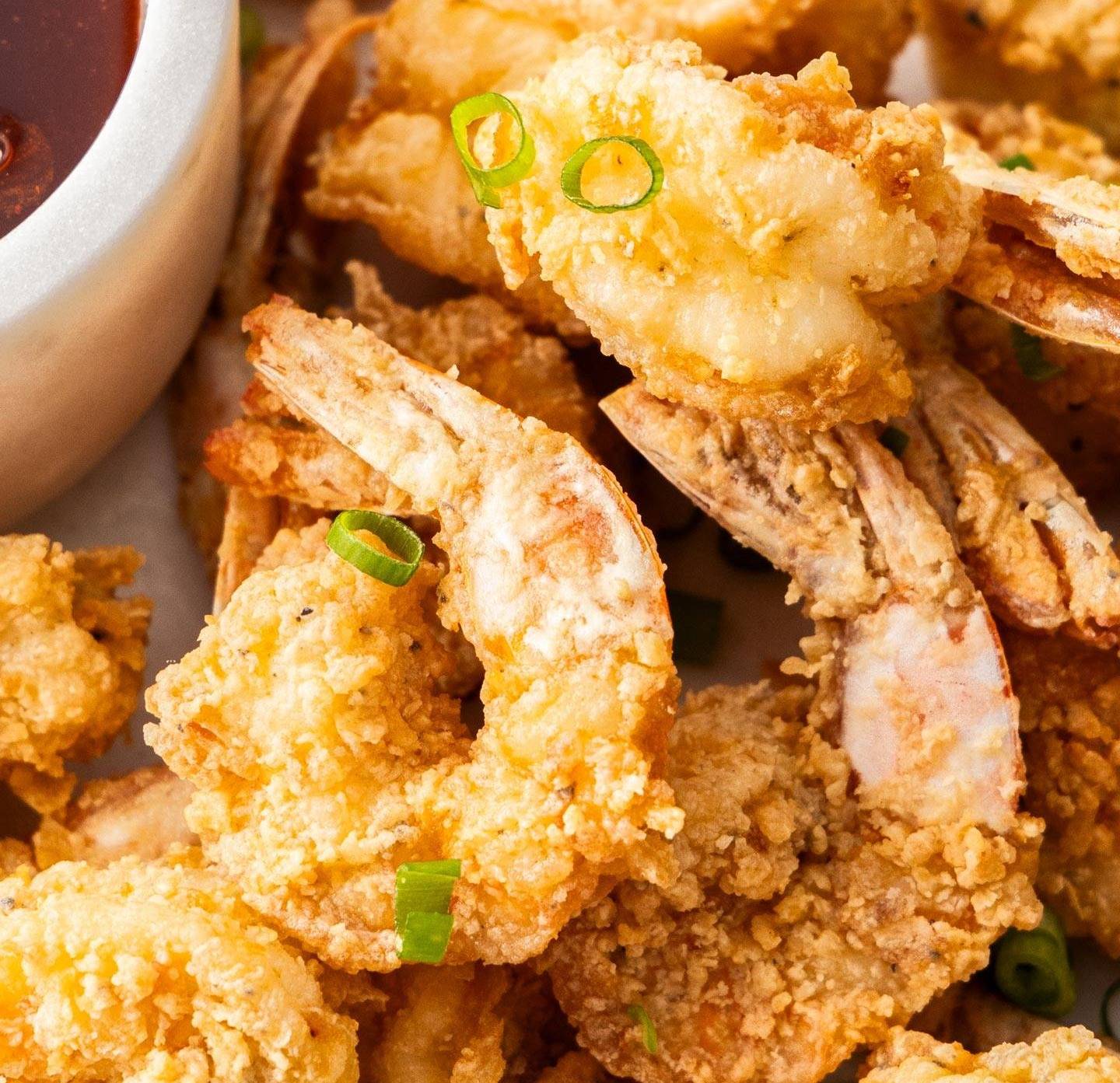 A pile of crispy prawns on a plate with a bowl of sauce next to them.