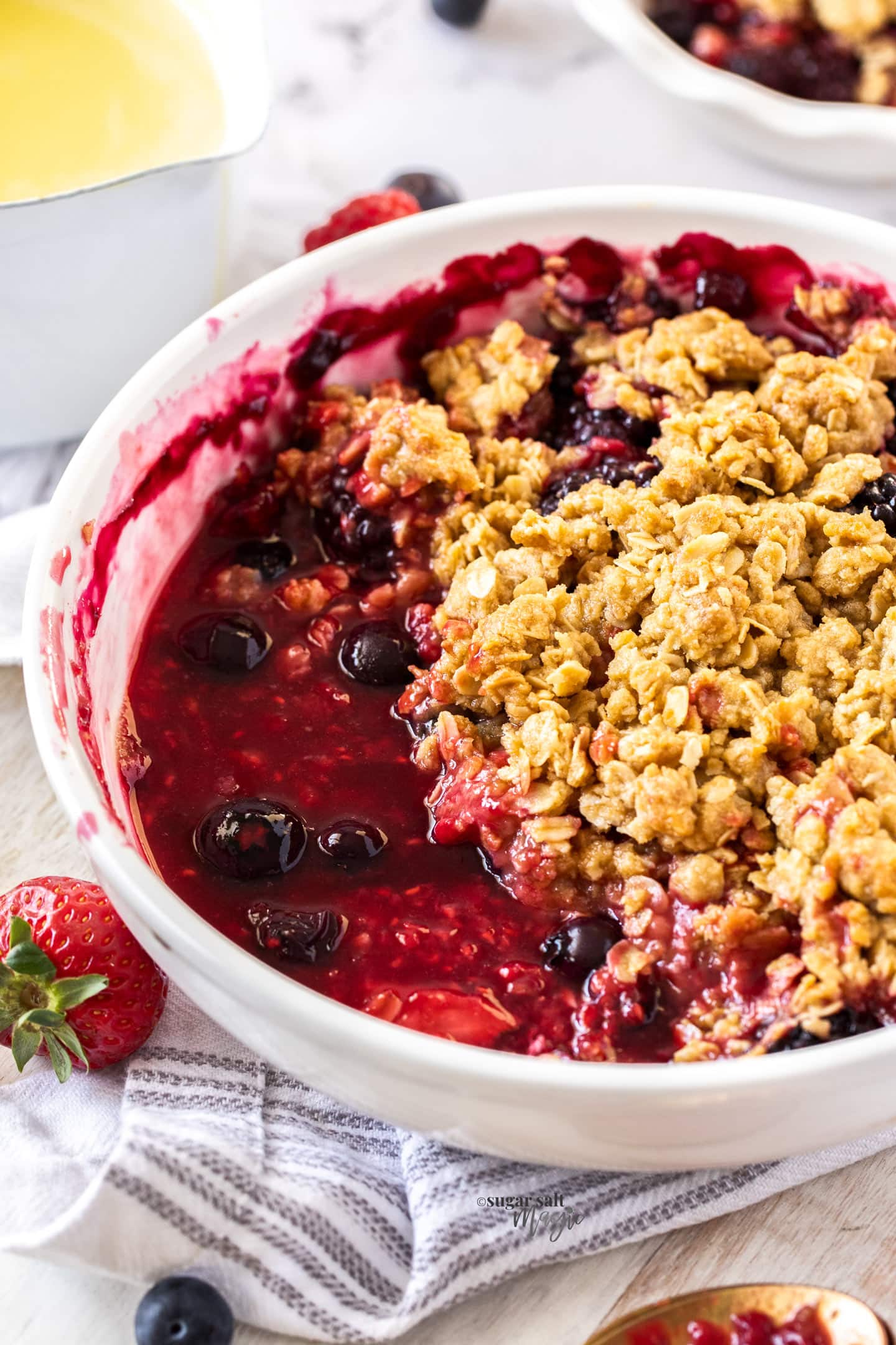 Angled view of a round dish filled with cooked berries topped with crumble.