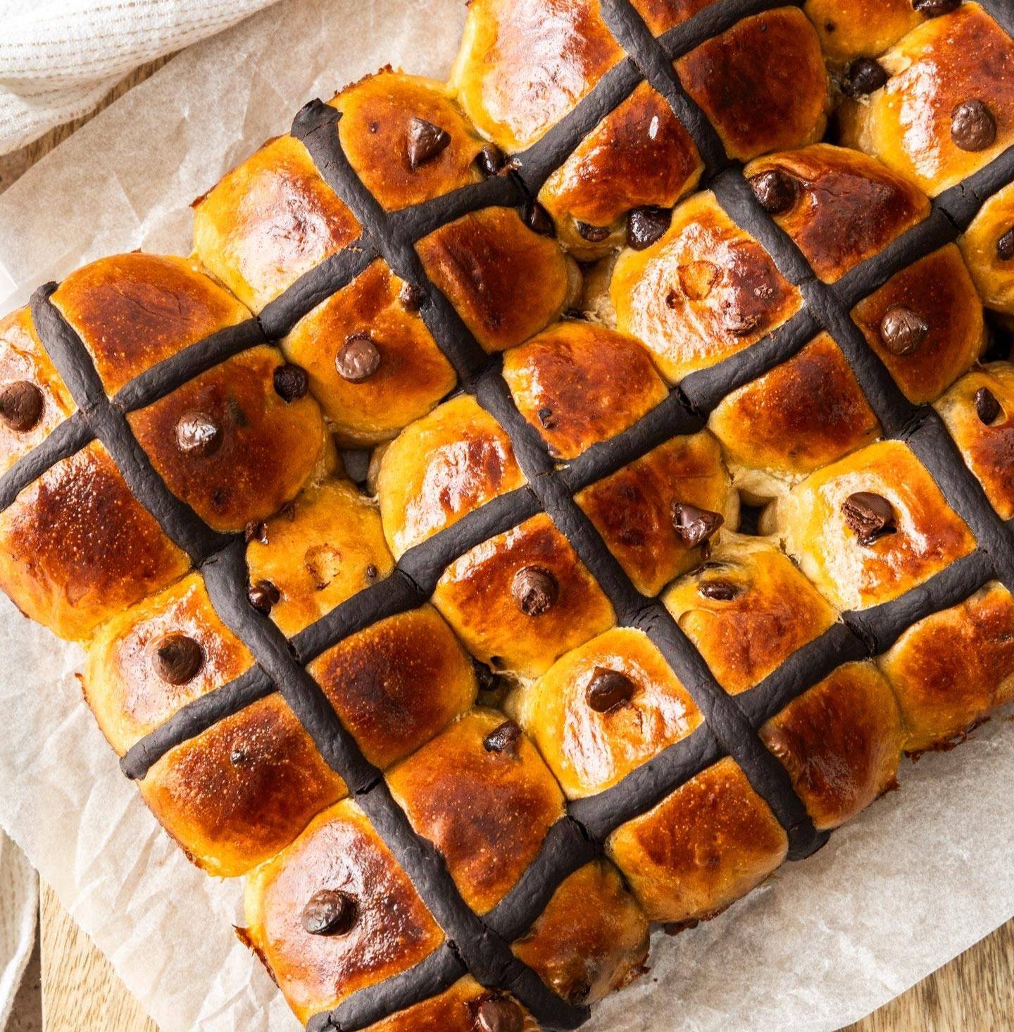 Top down view of 9 chocolate chip hot cross buns on a wooden board.