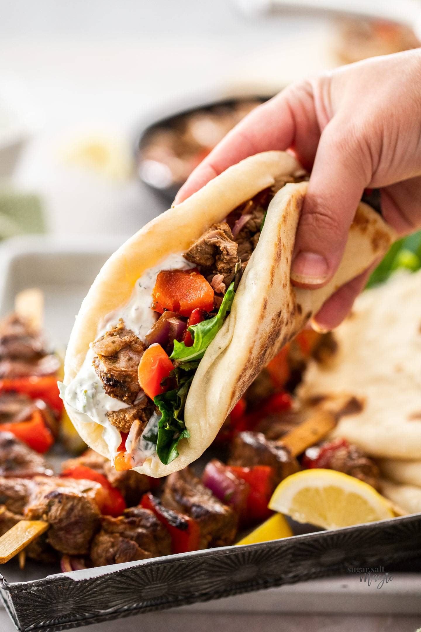 A hand holding a fluffy pita bread filled with lamb, vegetables and tzatziki.