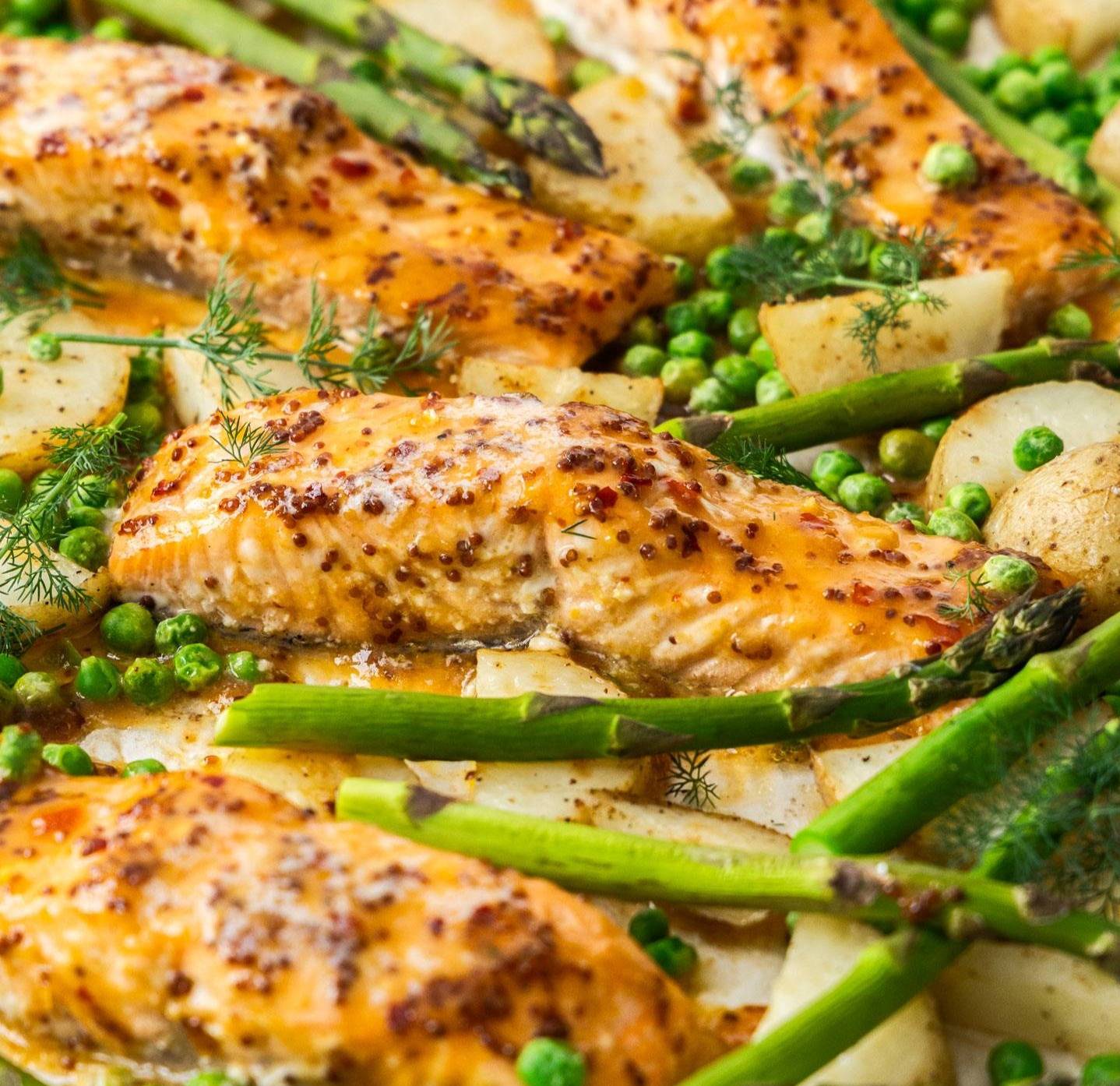 Closeup of a salmon fillet surrounded by peas and asparagus.