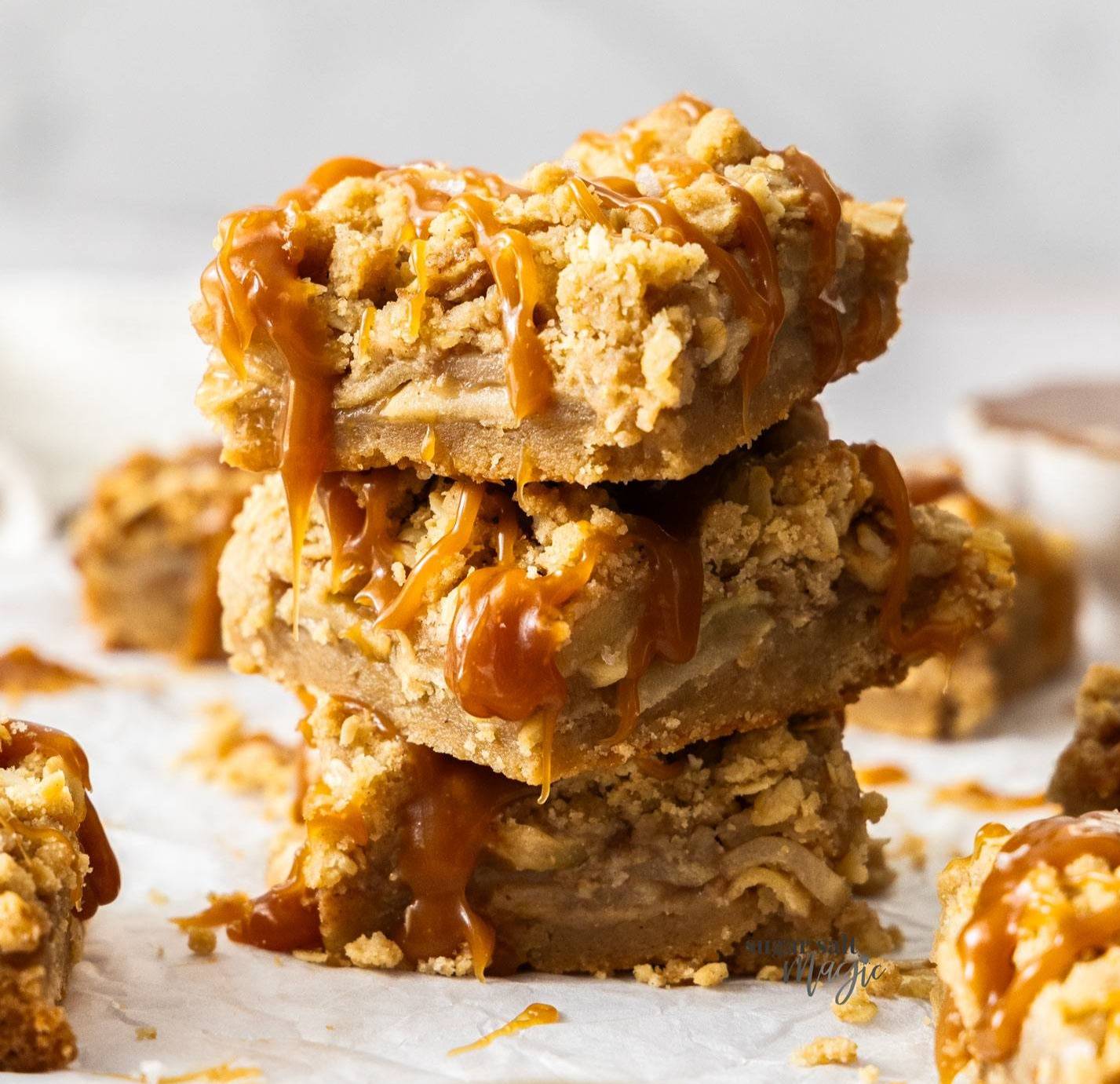 A stack of 3 caramel apple pie bars with caramel oozing down.