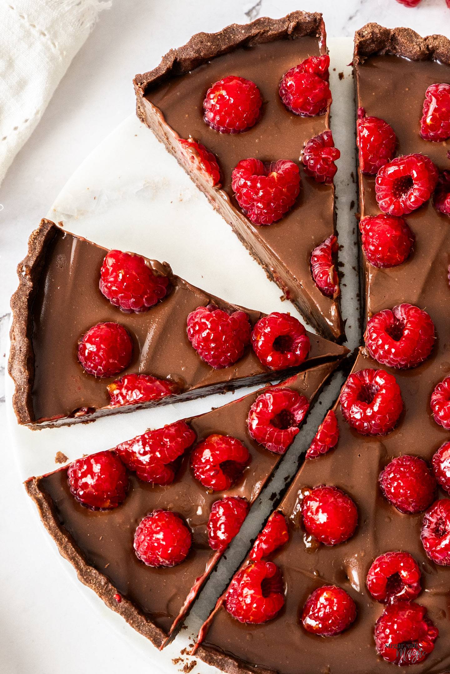 Top down view of a chocolate tart topped with raspberries, cut into wedges.