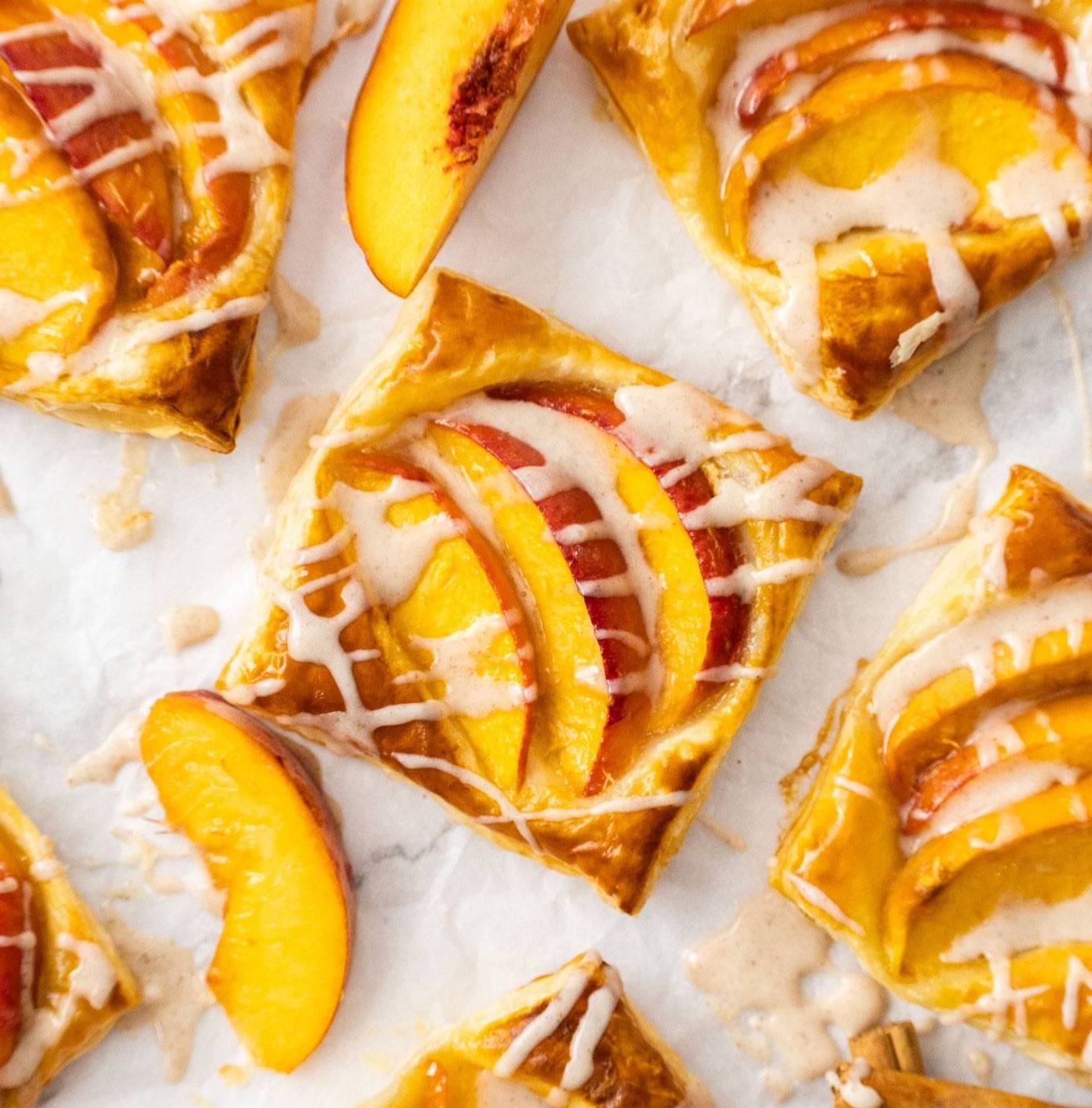 Top down view of a square peach tart on a sheet of baking paper.