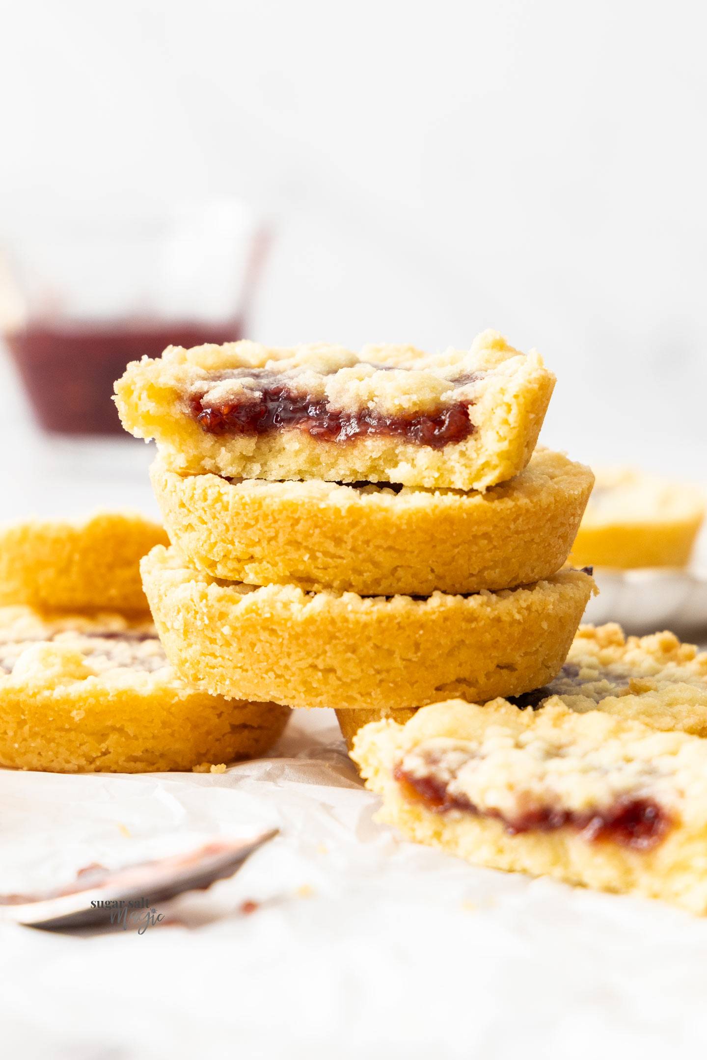 A stack of 3 raspberry crumble cookies with the top one broken in half to show the filling.