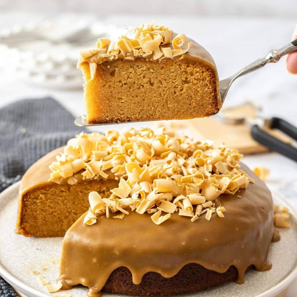 A slice of caramel mud cake being lifted from a full cake.