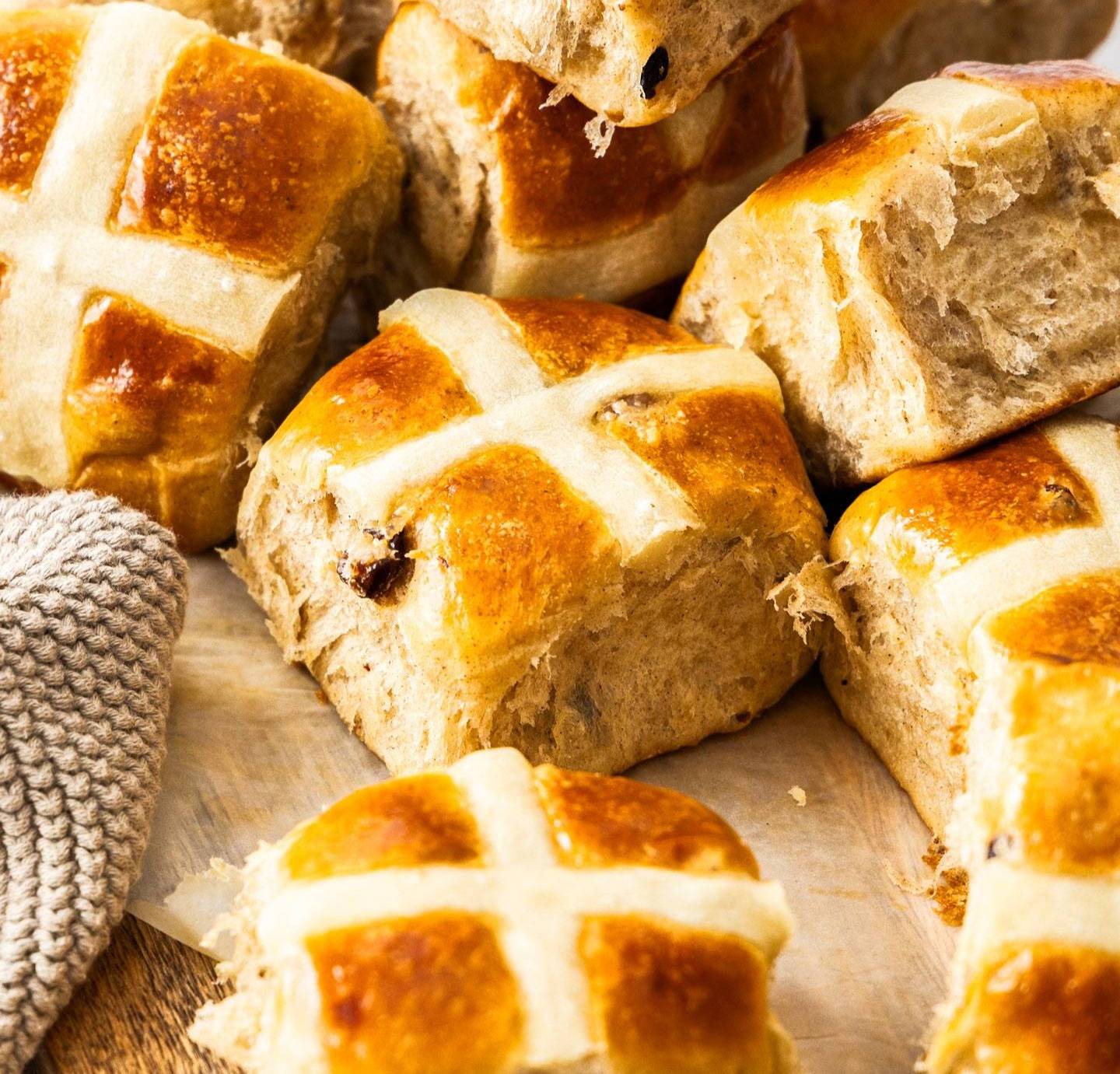 A pile of hot cross buns on a wooden platter.