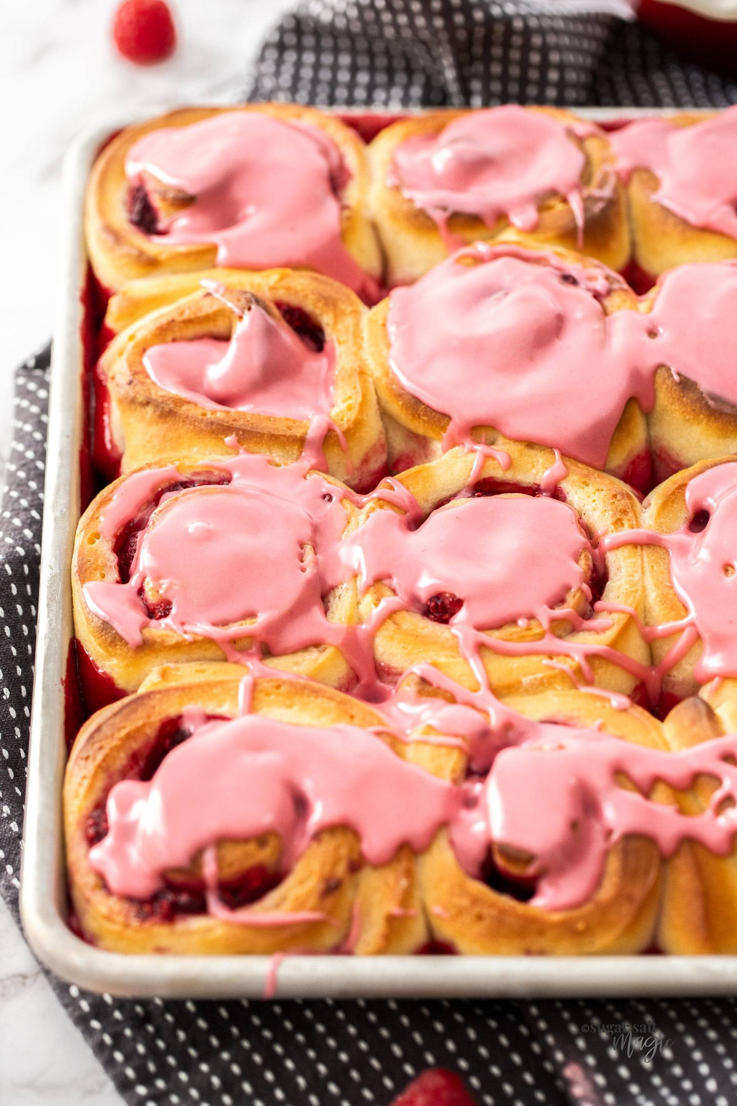 A batch of raspberry cinnamon rolls with a pink raspberry icing.