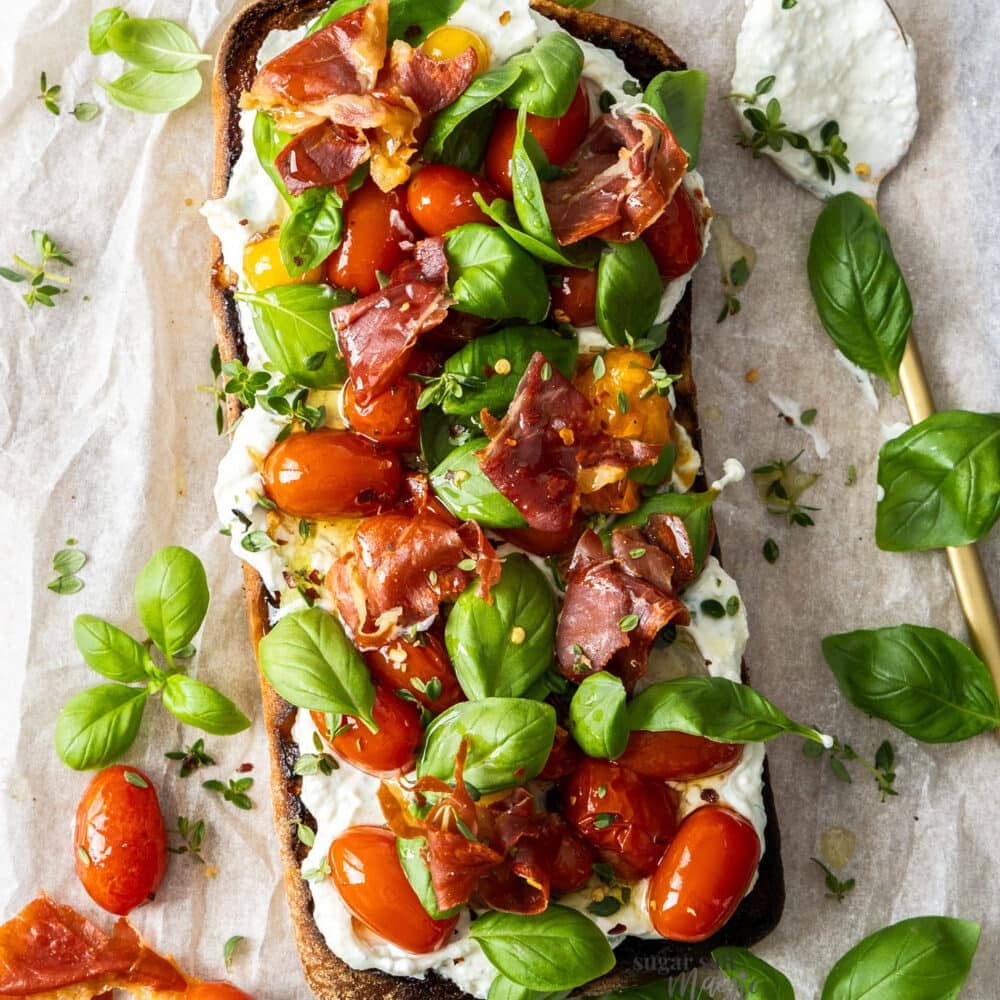 Top down view of a half ciabatta loaf topped with ricotta, tomatoes and basil.
