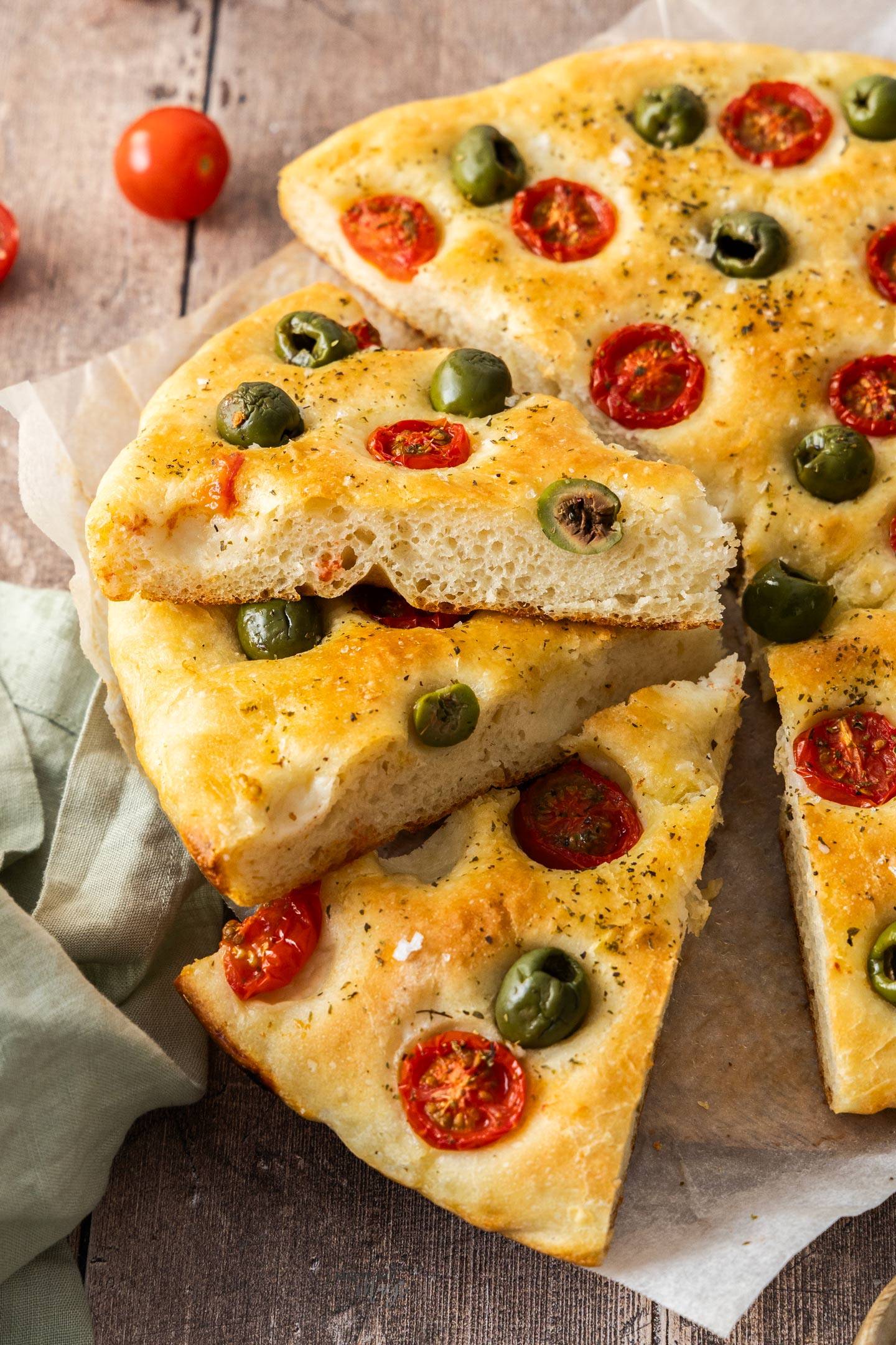 Wedges of focaccia barese stacked on top of each other next to the rest of the focaccia.