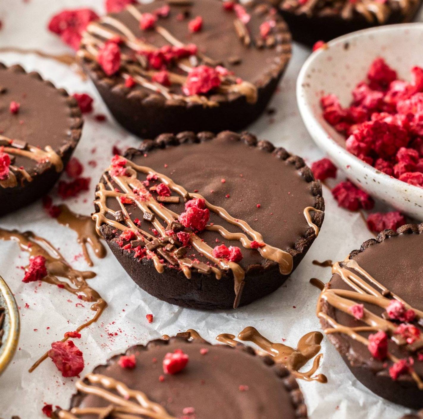 Mini chocolate tarts topped with a drizzle of chocolate and pieces of freeze dried raspberry.