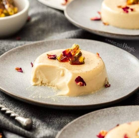 A panna cotta on a plate topped with pistachios and rose petals.