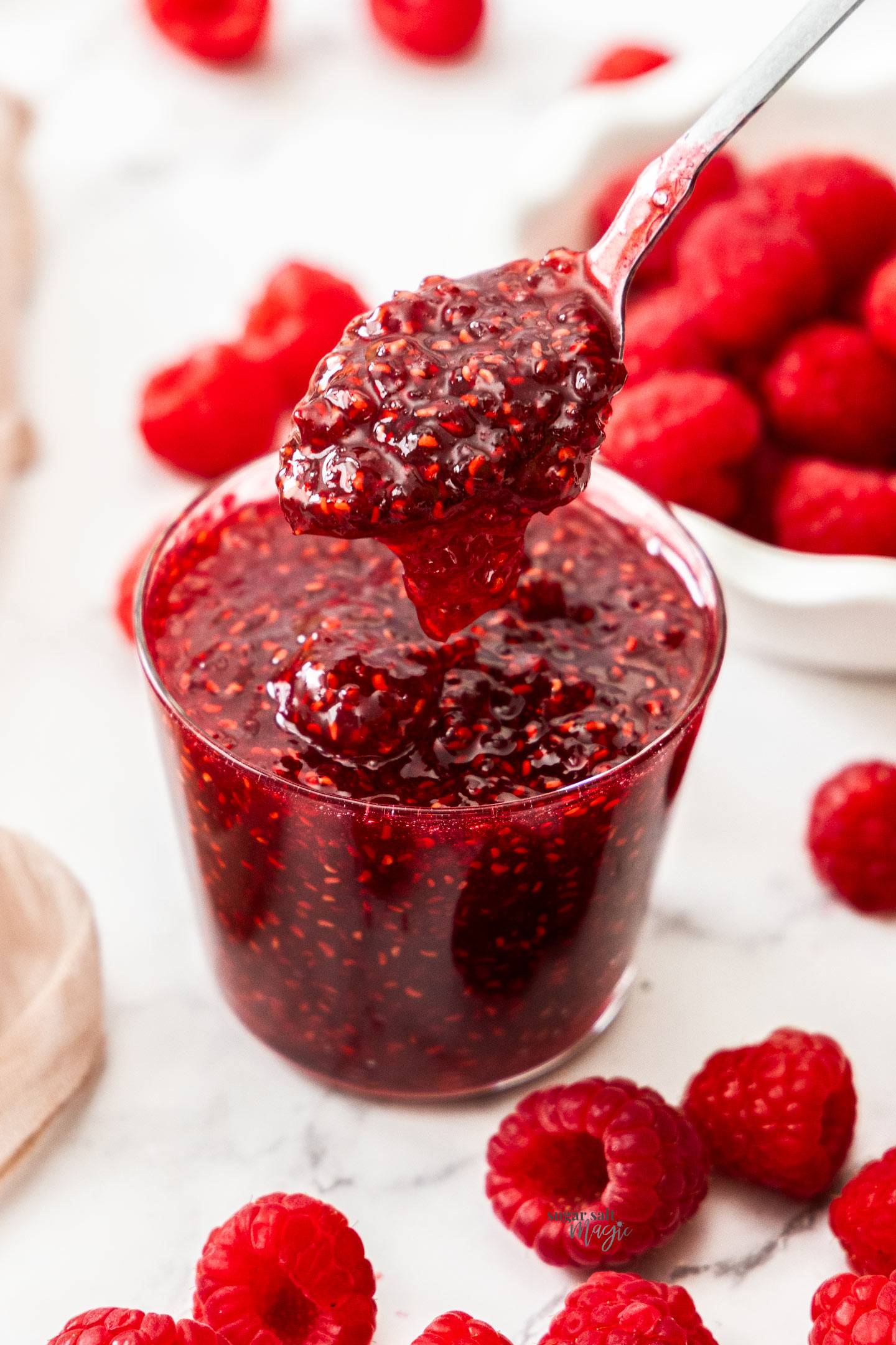 A spoon taking raspberry jam out of a glass.