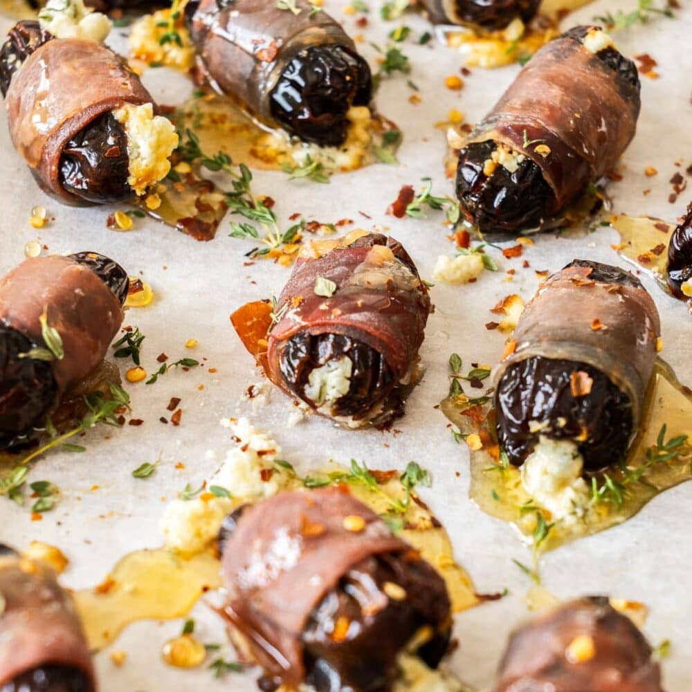 Prosciutto wrapped dates on a tray drizzled with hot honey.