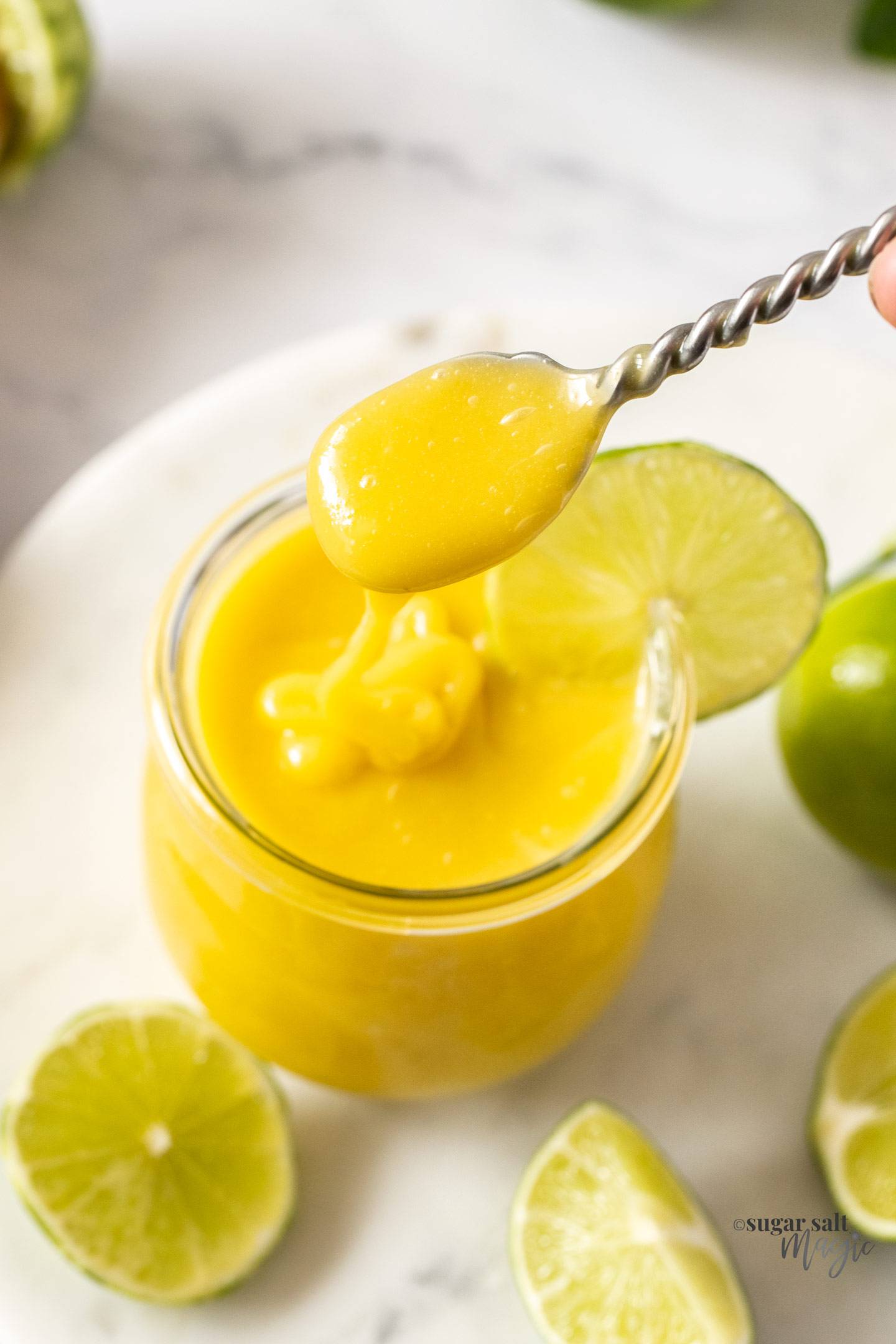 A spoon scooping lime curd from a jar.
