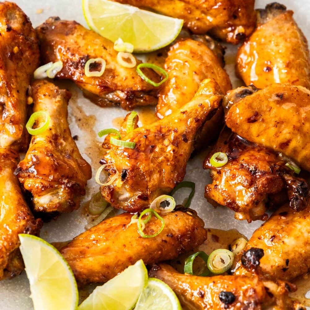 A pile of hot honey chicken wings with some wedges of lime.