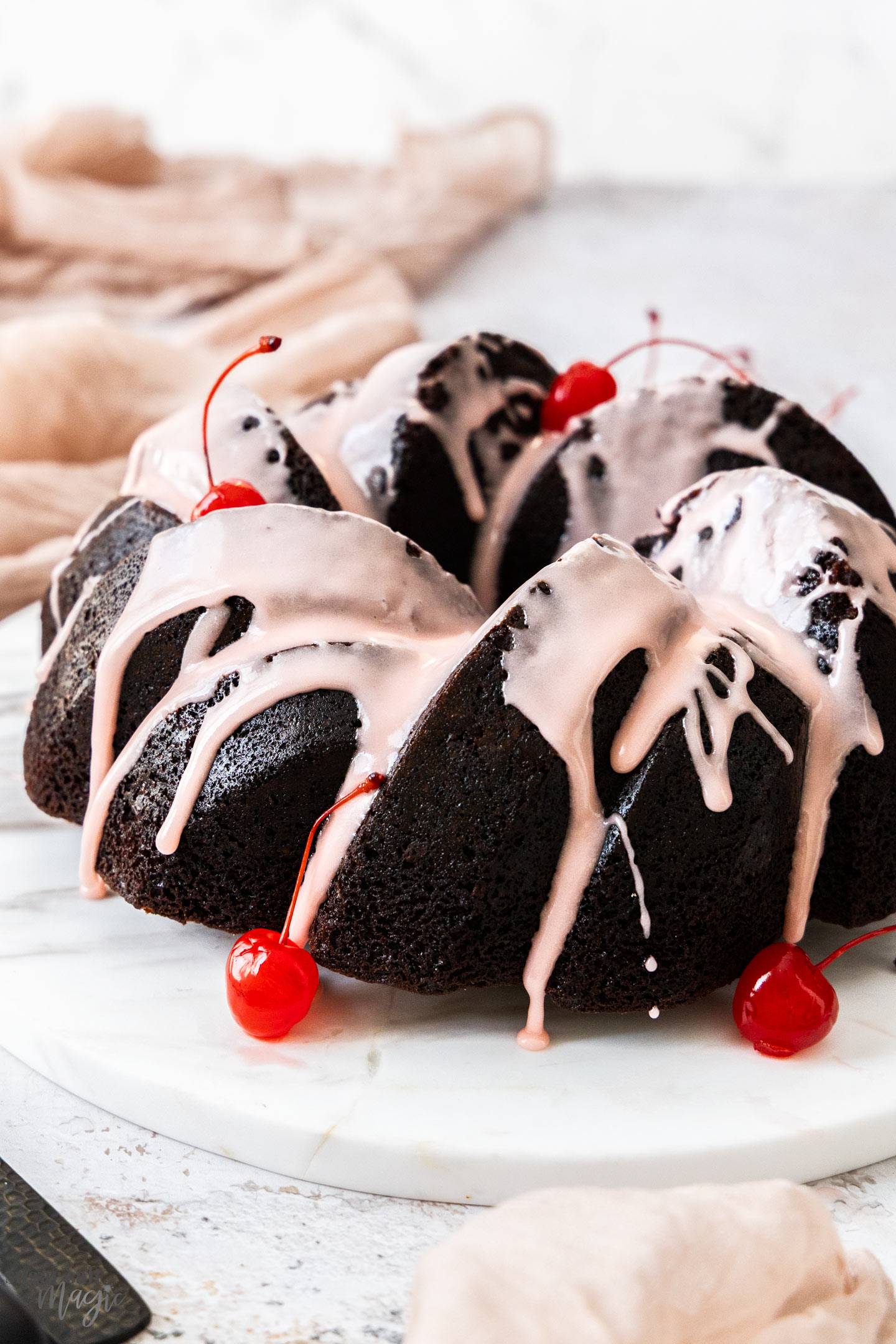 A whole chocolate bundt cake topped with cherry icing on a marble platter.