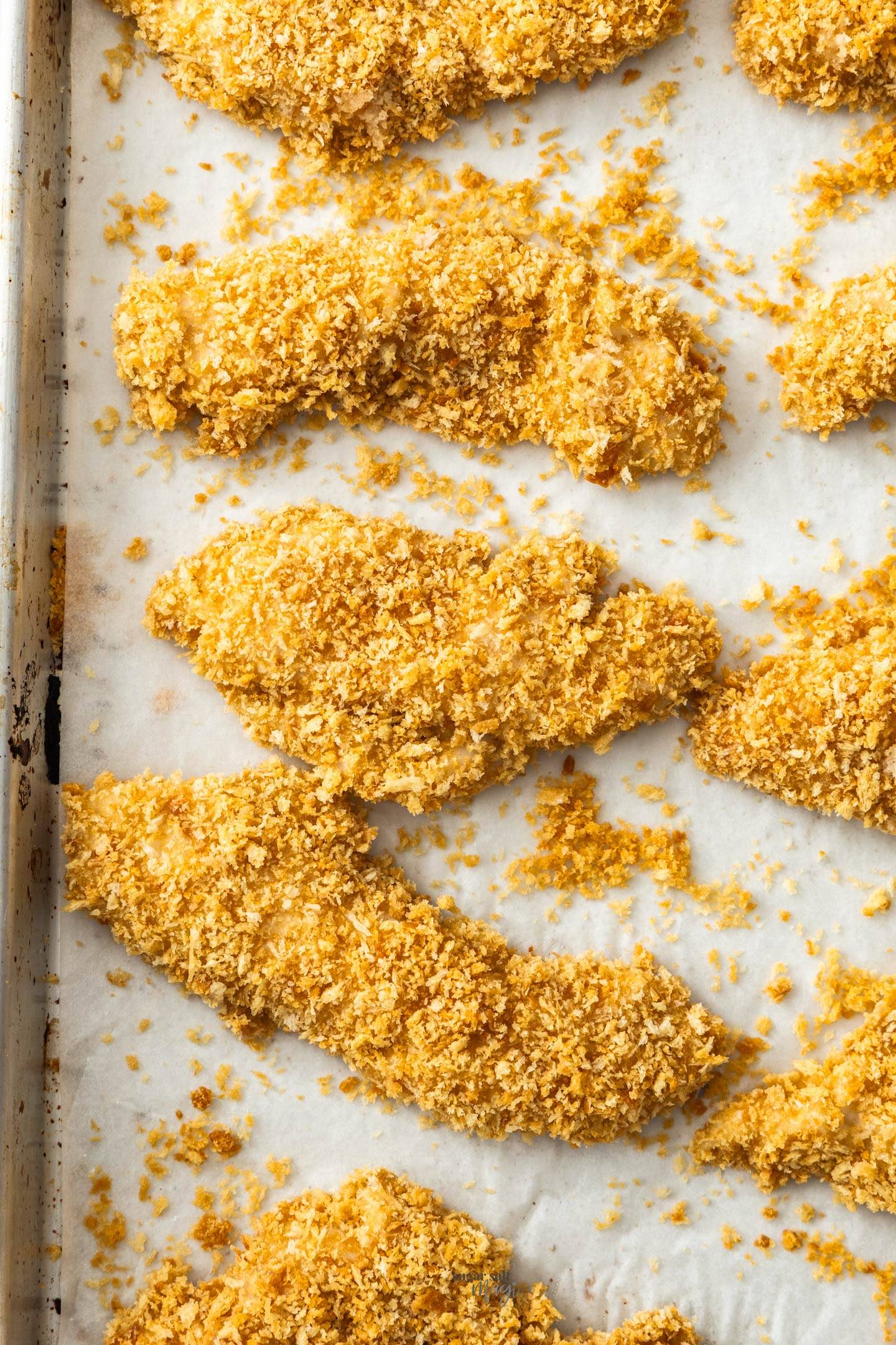 Top down view of crumbed chicken tenders on a baking tray.