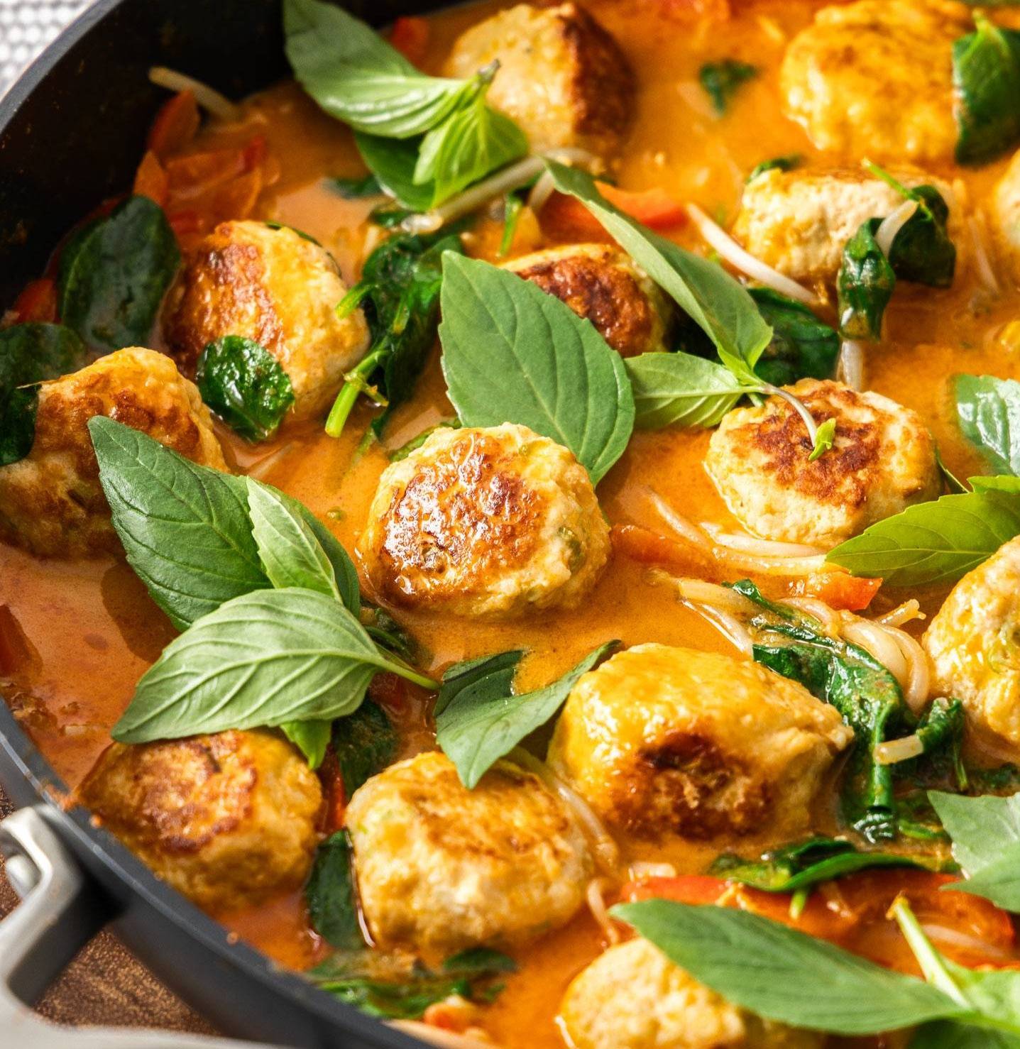 Meatballs in a red curry sauce in a pan.