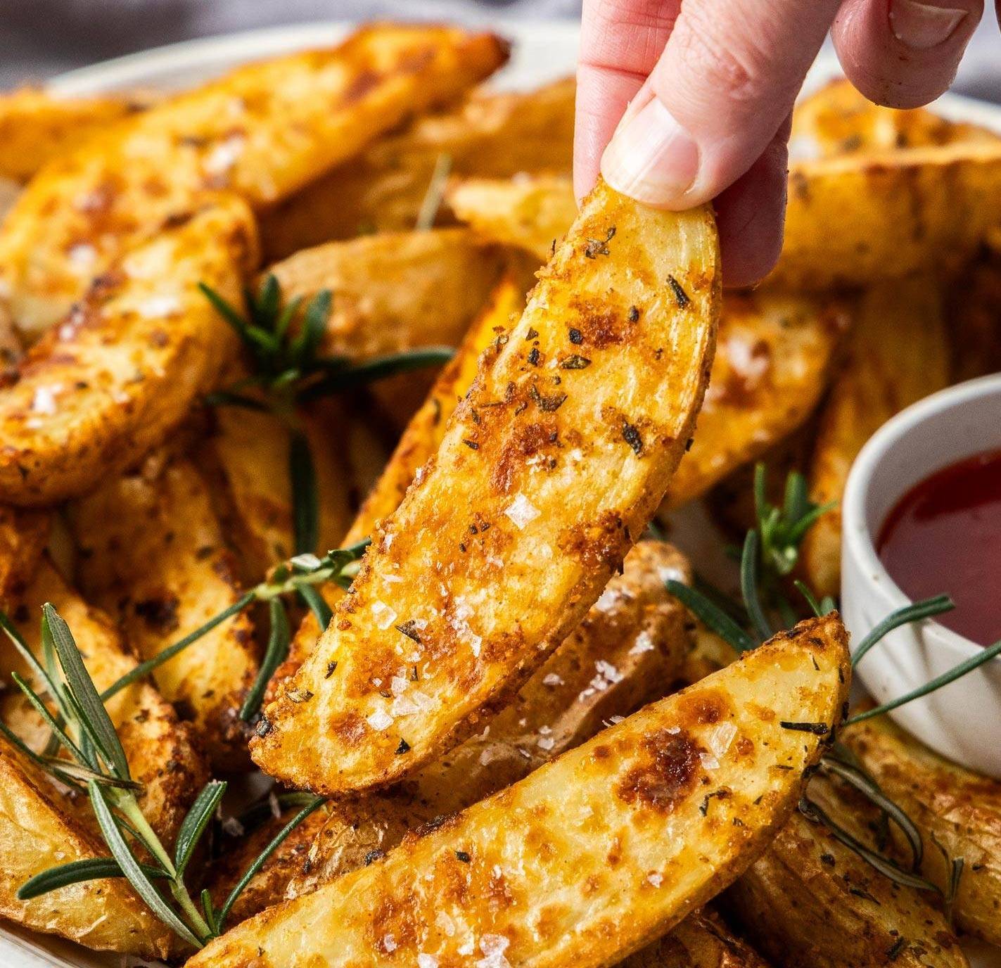 A hand taking a potato wedge from a pile.