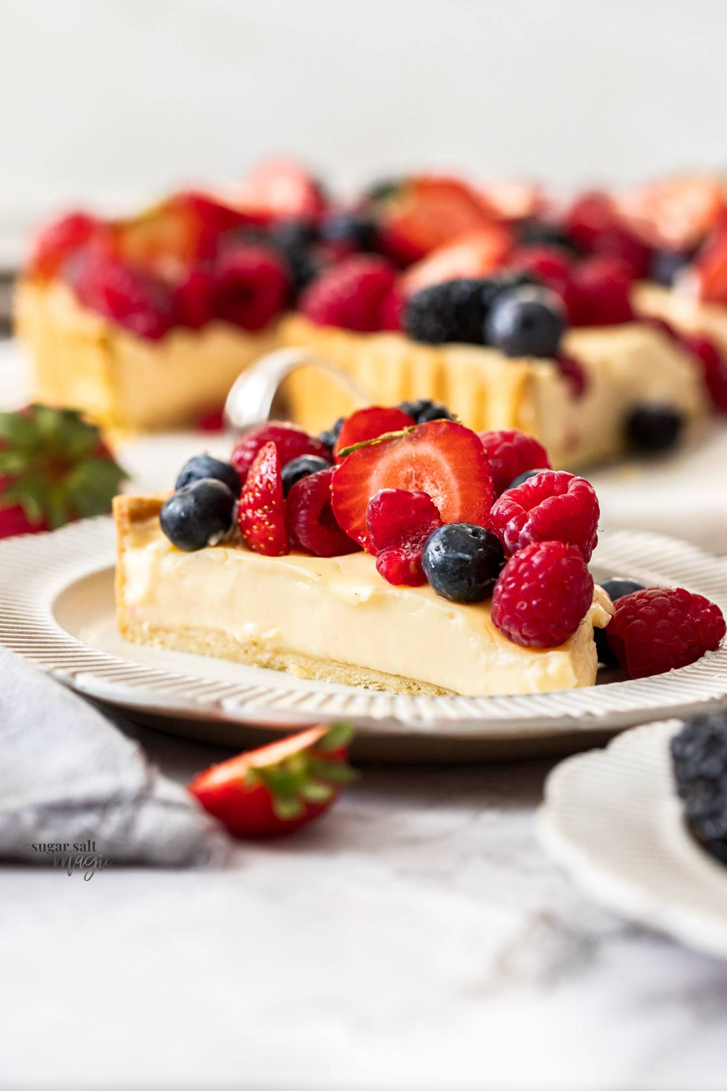 A slice of fruit custard tart topped with berries.
