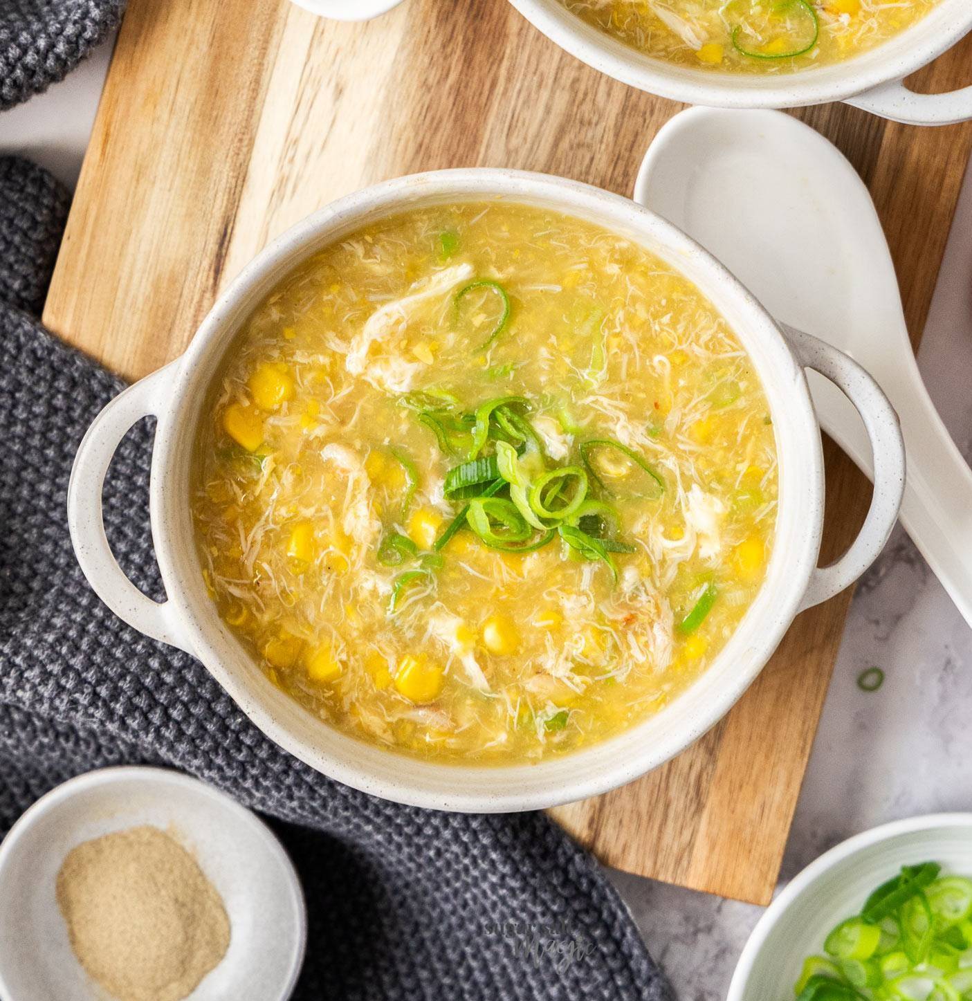 Top down view of a bowl of crab and sweetcorn soup on a wooden board.