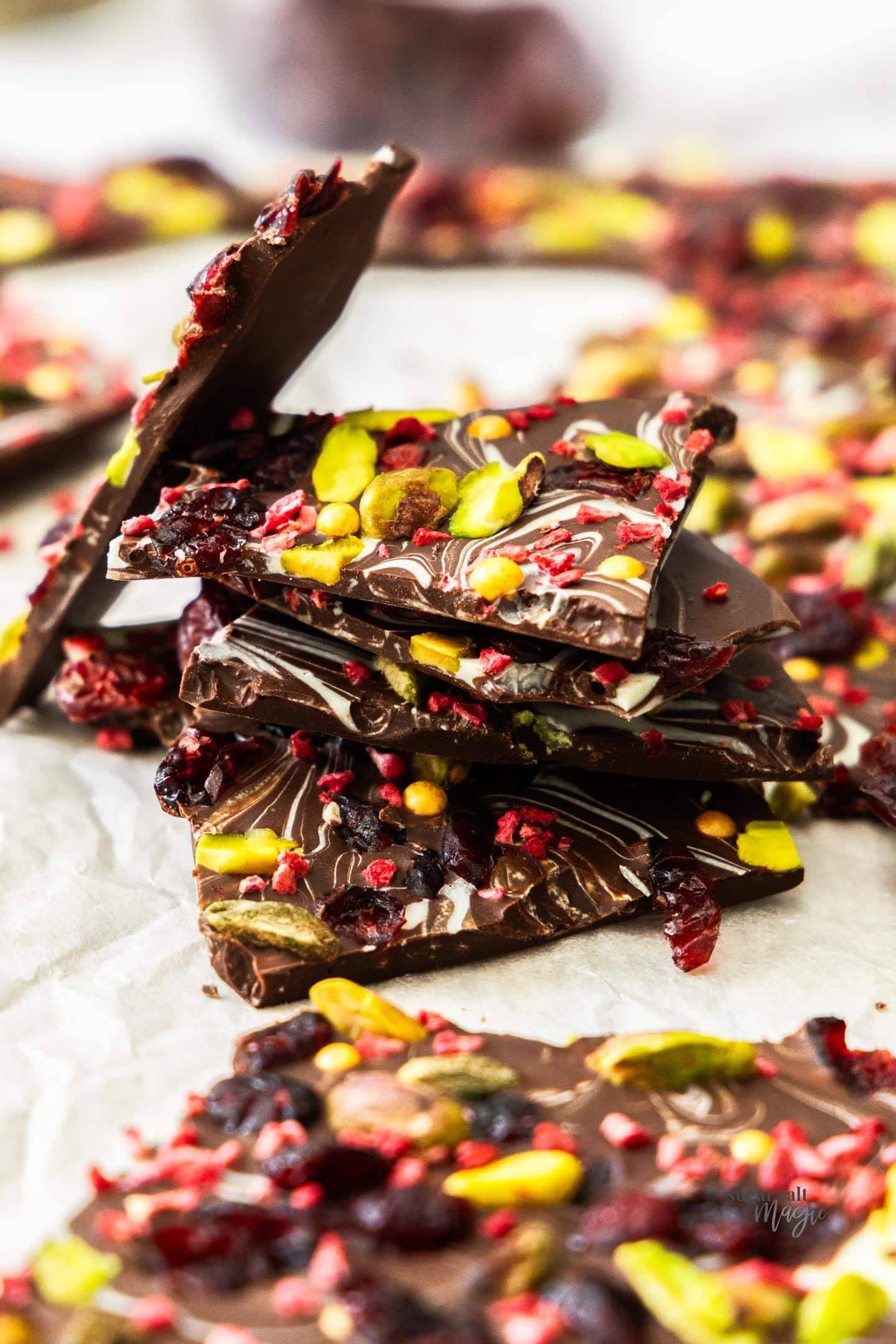 A stack of shards of chocolate bark topped with pistachios and cranberries.