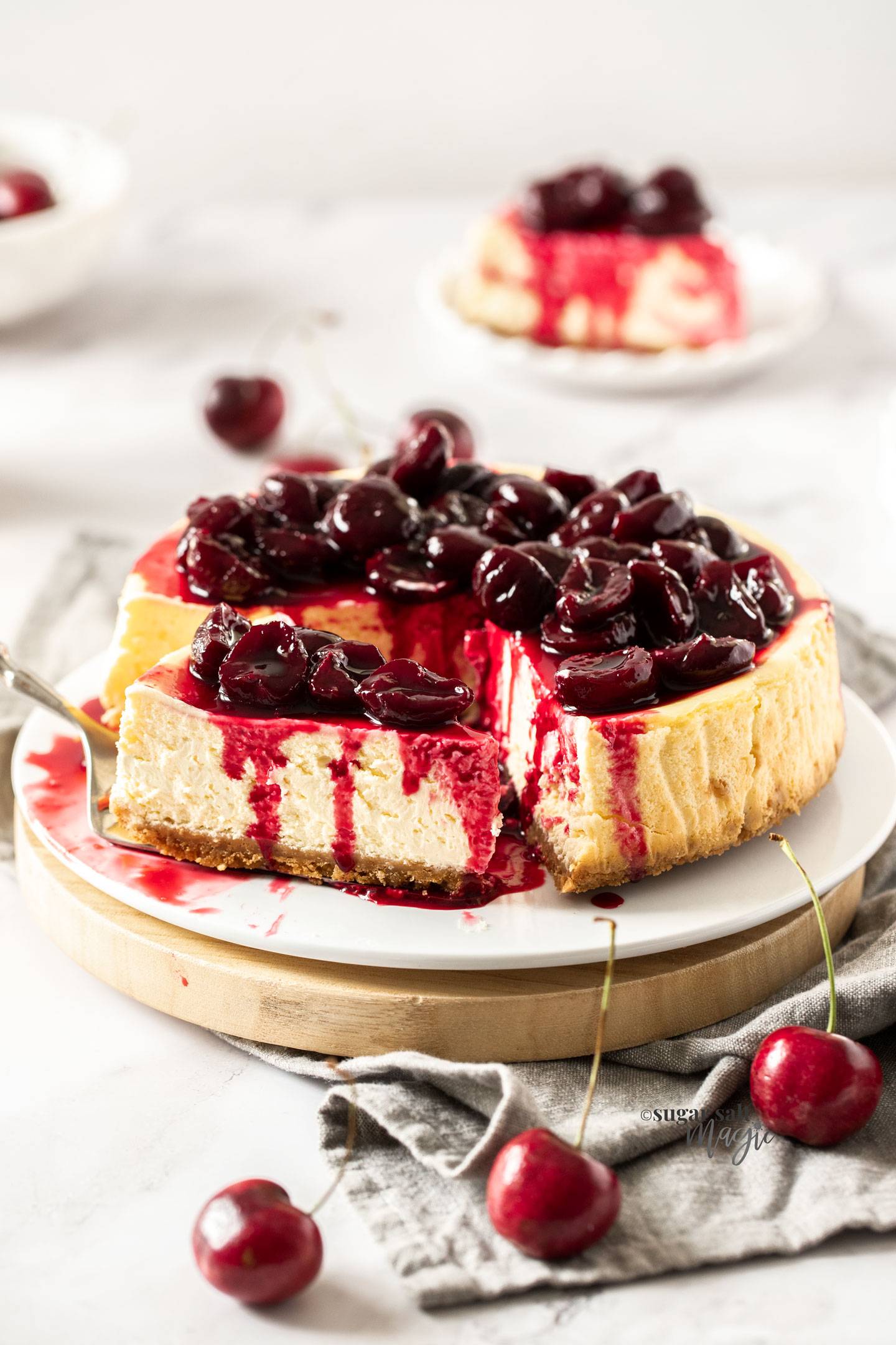 A cheesecake topped with cherries with a slice being removed.