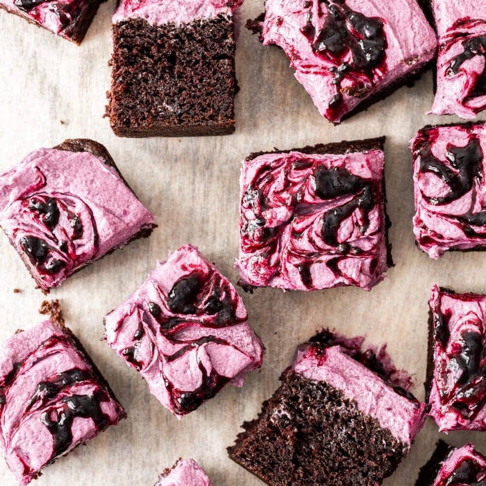 Squares of cake with blueberry frosting on a wooden board.