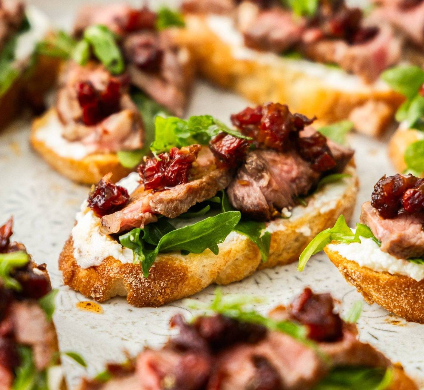 A batch of steak crostini on a platter.