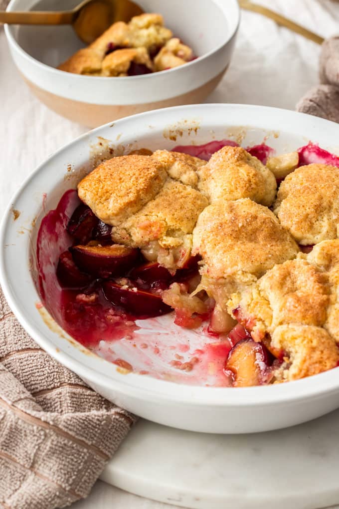 A pie dish filled with stewed apples, plums and cobbler topping.