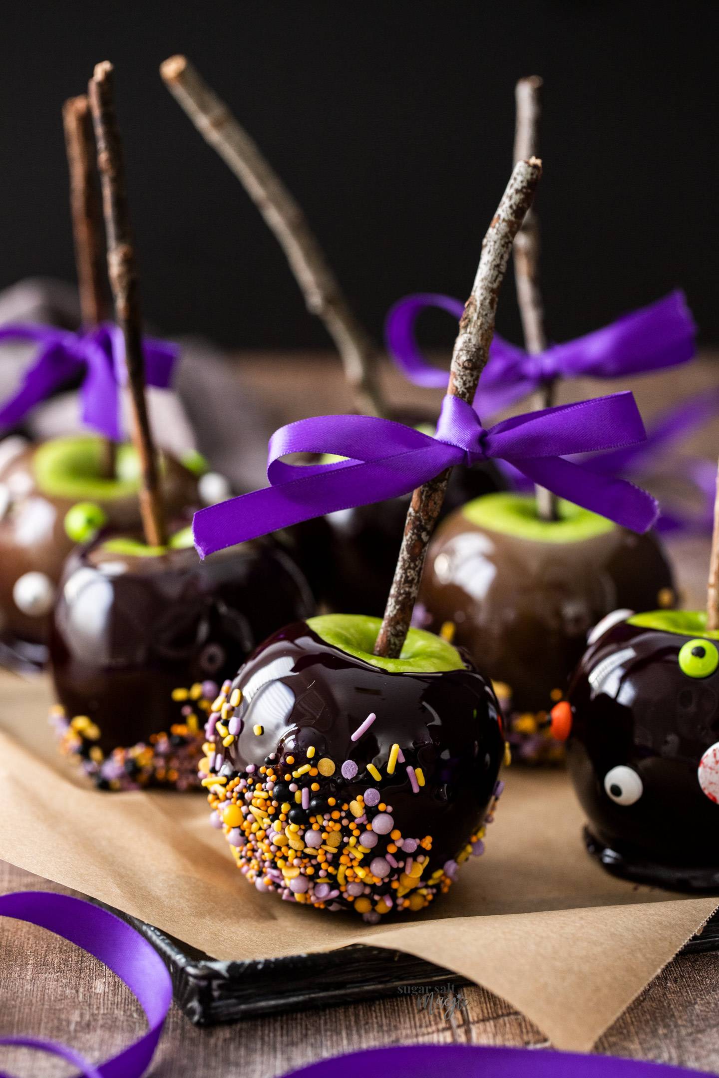 Black candy apples with sprinkles on a metal tray.