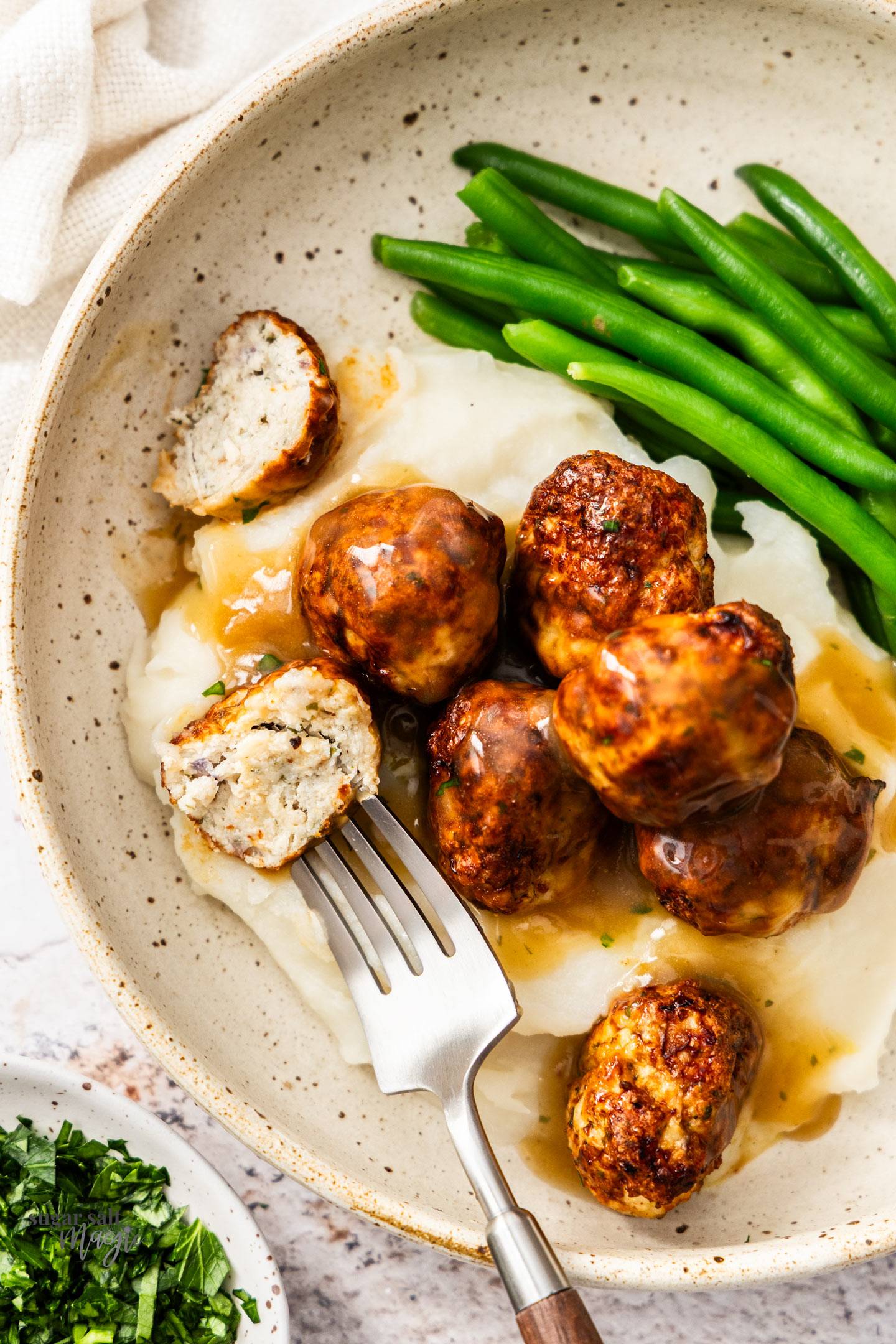 Top down view of chicken meatballs, mashed potato, gravy and green beans in a bowl.