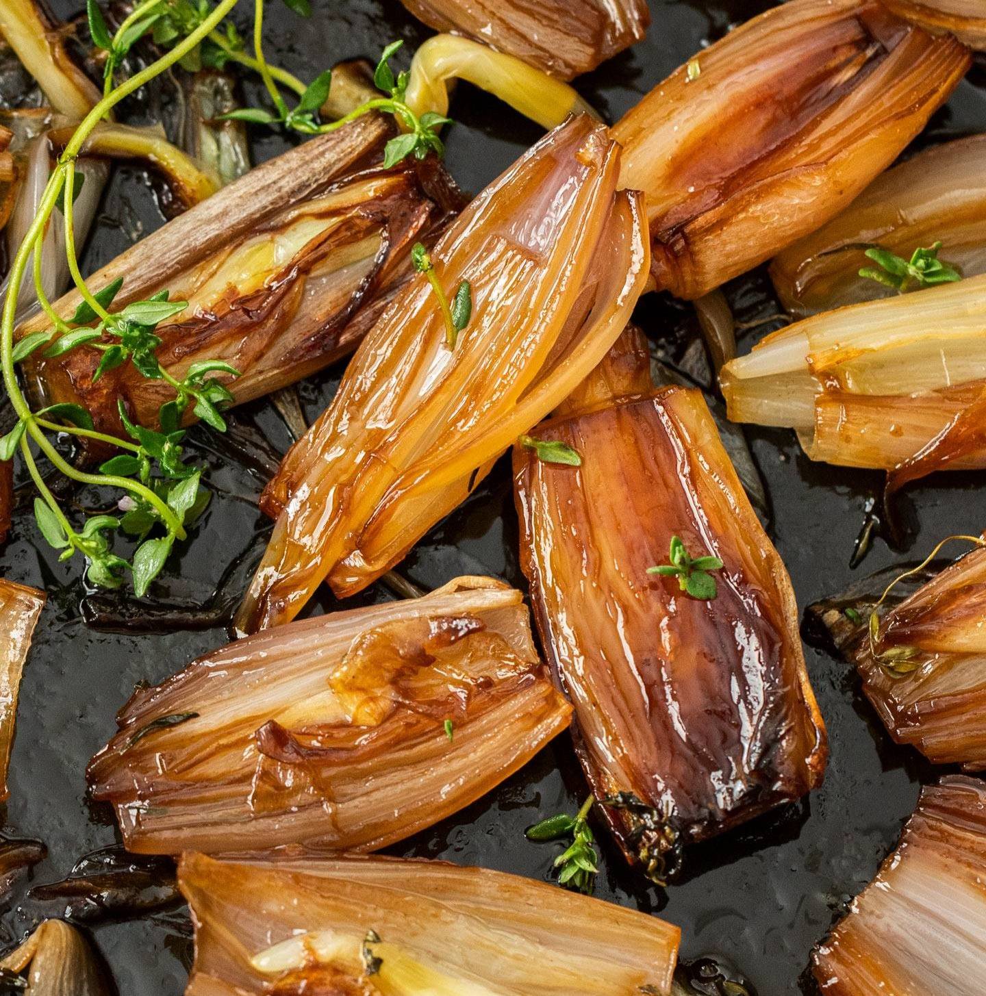 Caramelised roasted shallots in a cast iron pan with fresh thyme leaves.
