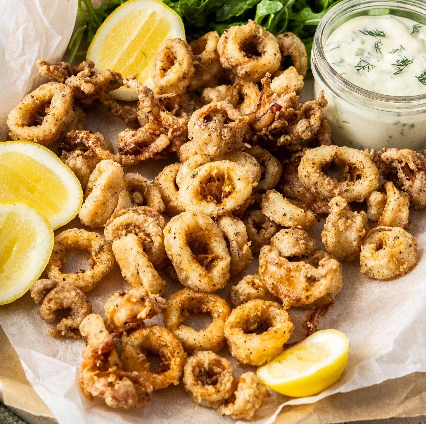 A pile of fried squid rings surrounded by wedges of lemon.