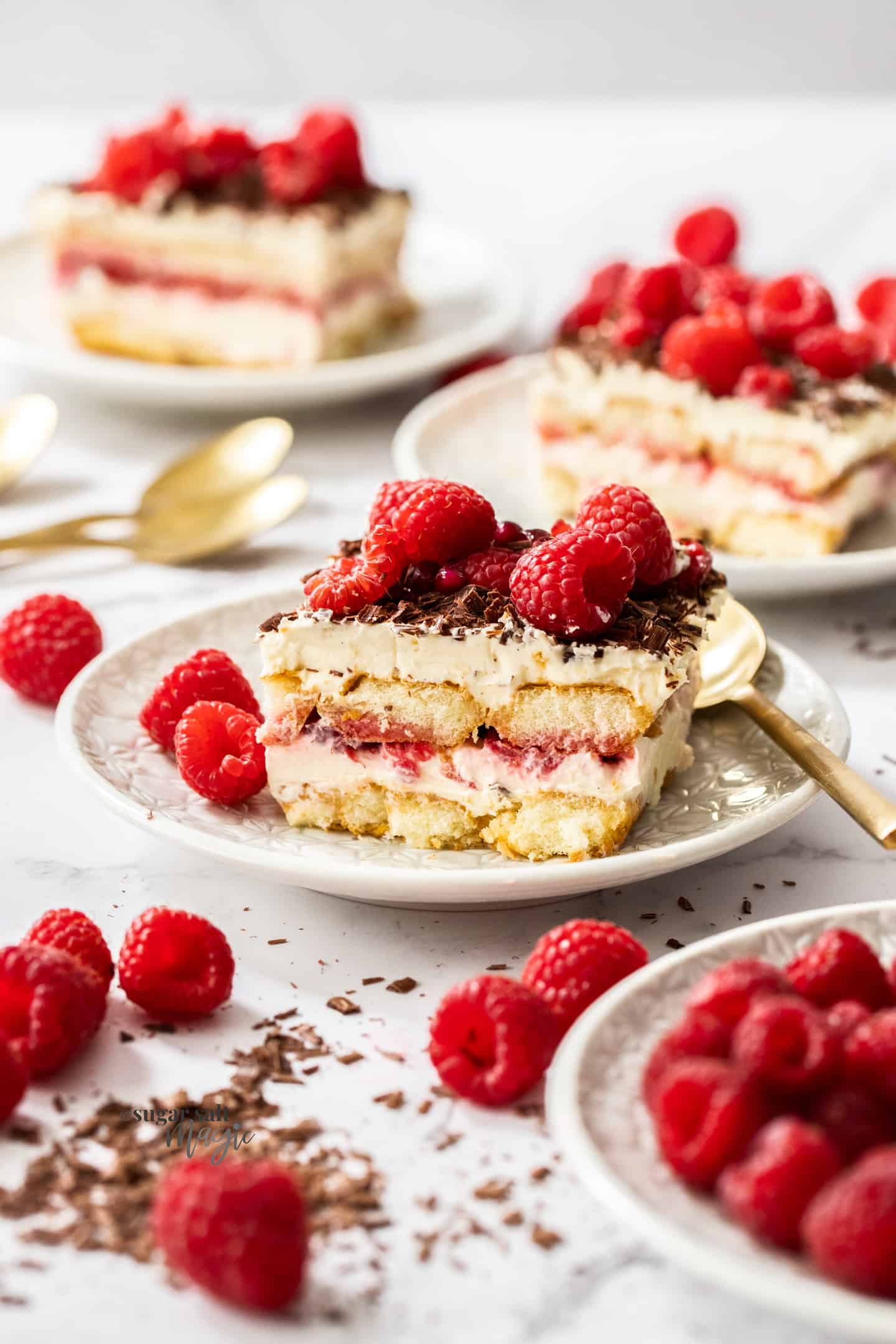 A slice of raspberry tiramisu on a dessert plate with more in the background.