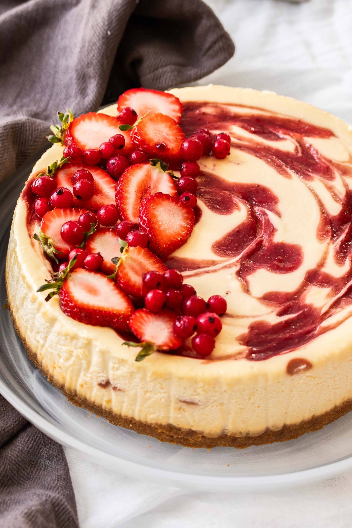 Angled image of a whole strawberry swirl cheesecake on a glass dish.