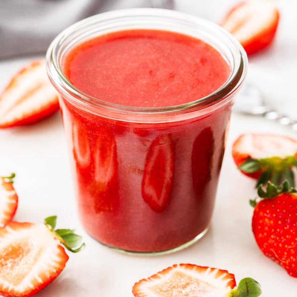 A jar filled to the top with strawberry sauce.
